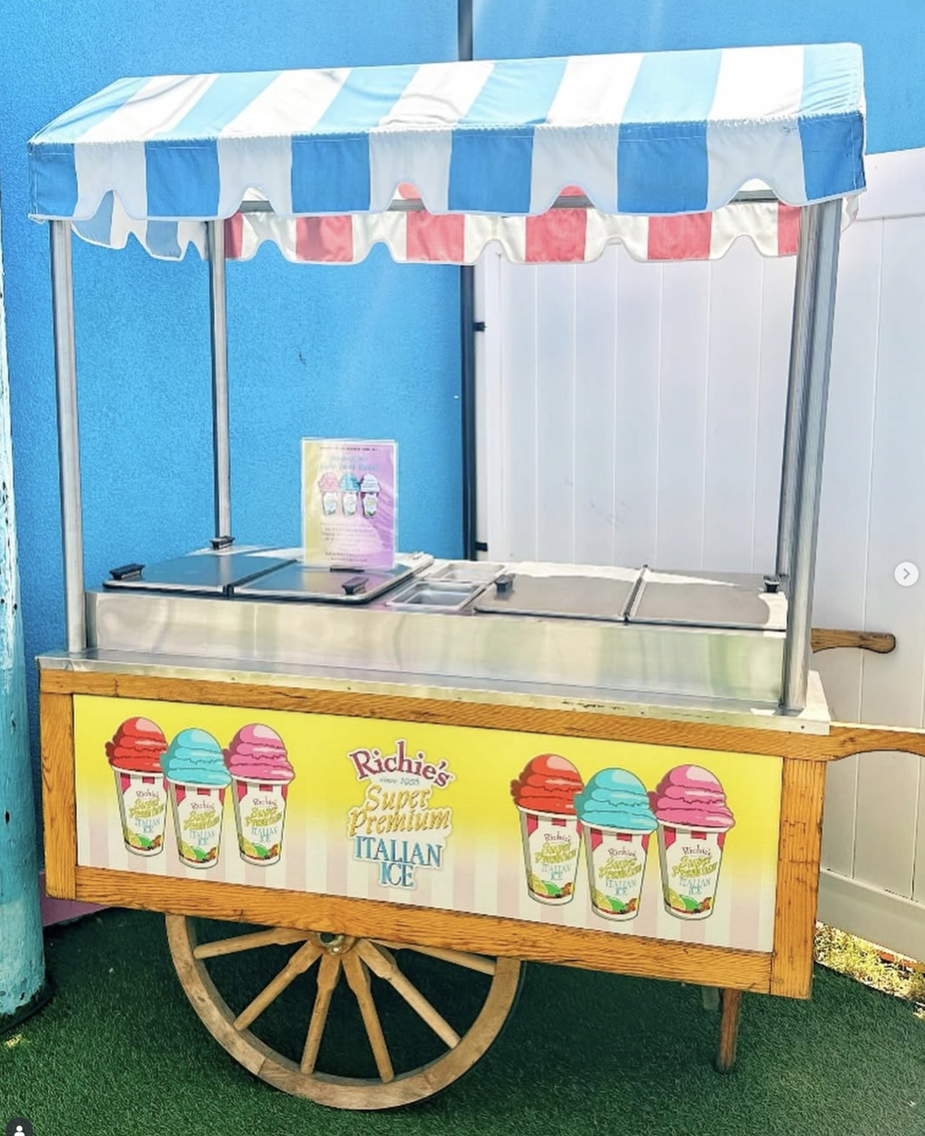 Ice cream cart with a yellow front decorated with images of ice cream cones and the words 'Richie's Super Premium Italian Ice'.