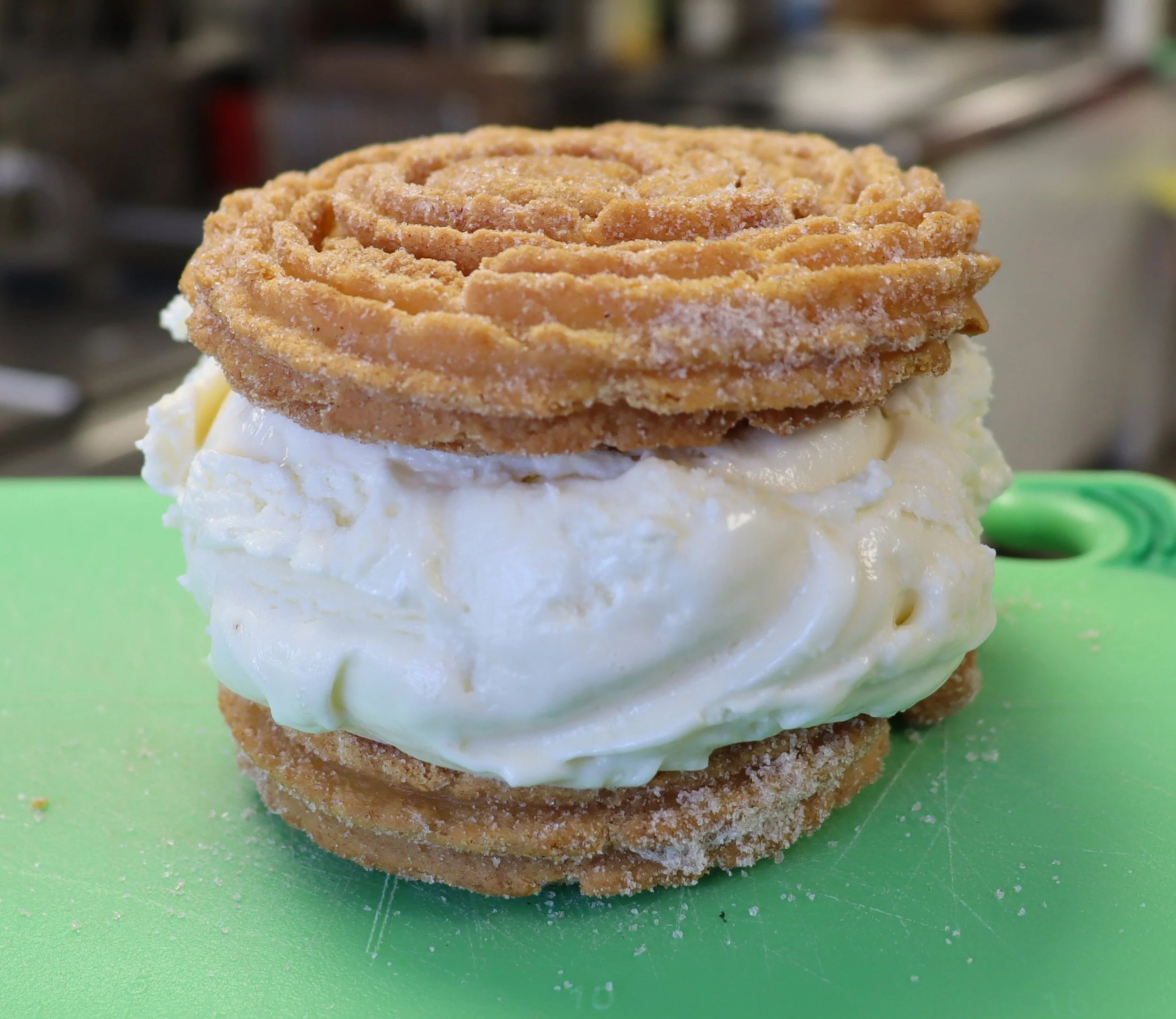 Close-up of a dessert with two crispy, spiral cookies on top of cream and cake layers, placed on a green surface.