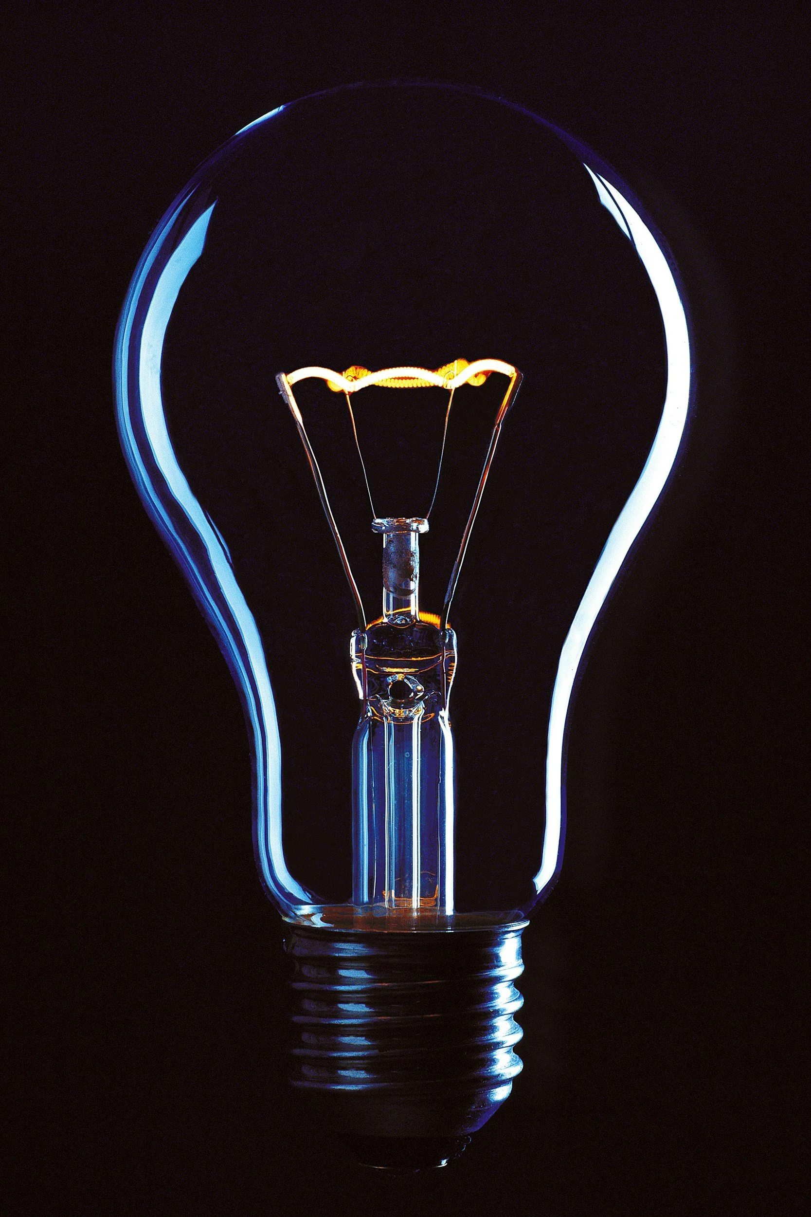 Close-up of an incandescent light bulb with a glowing filament against a black background.
