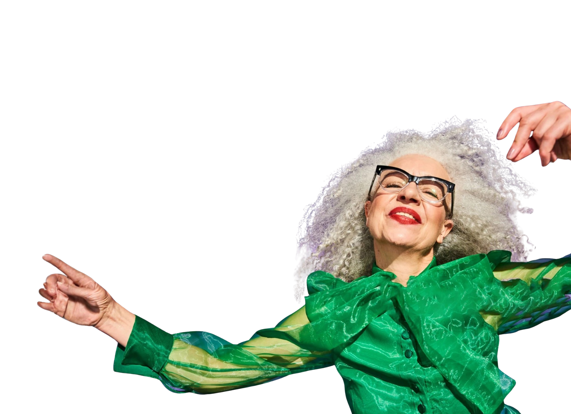 Older woman with curly grey hair, glasses, and bright red lipstick smiling, wearing a green shiny outfit, her hand are in the air as though she is dancing