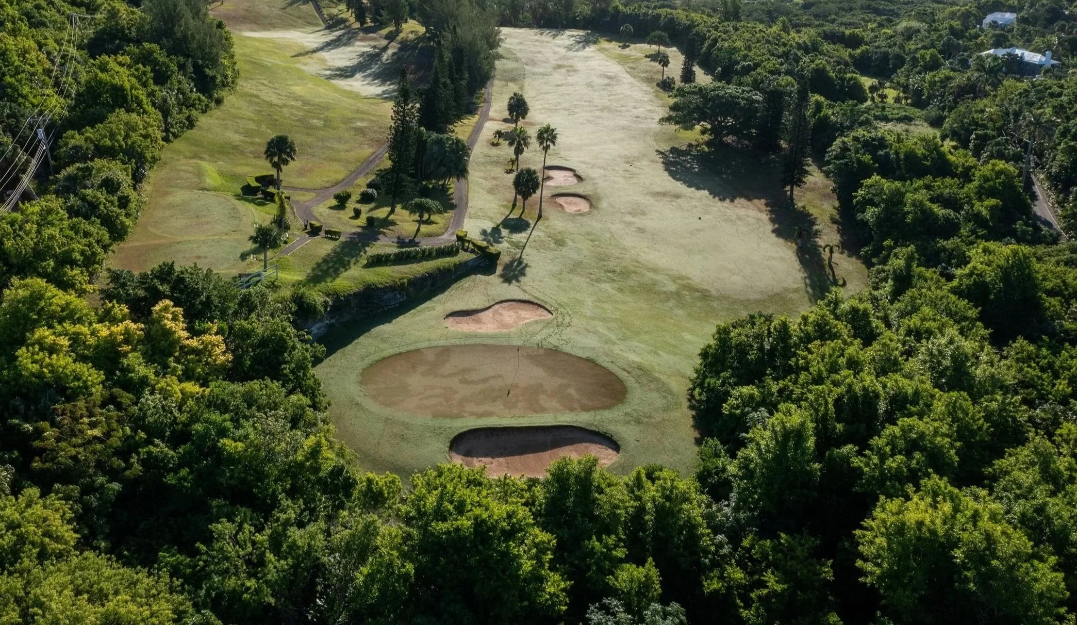 An aerial view of a golf course with several sand traps, surrounded by dense green trees and a few pathways.