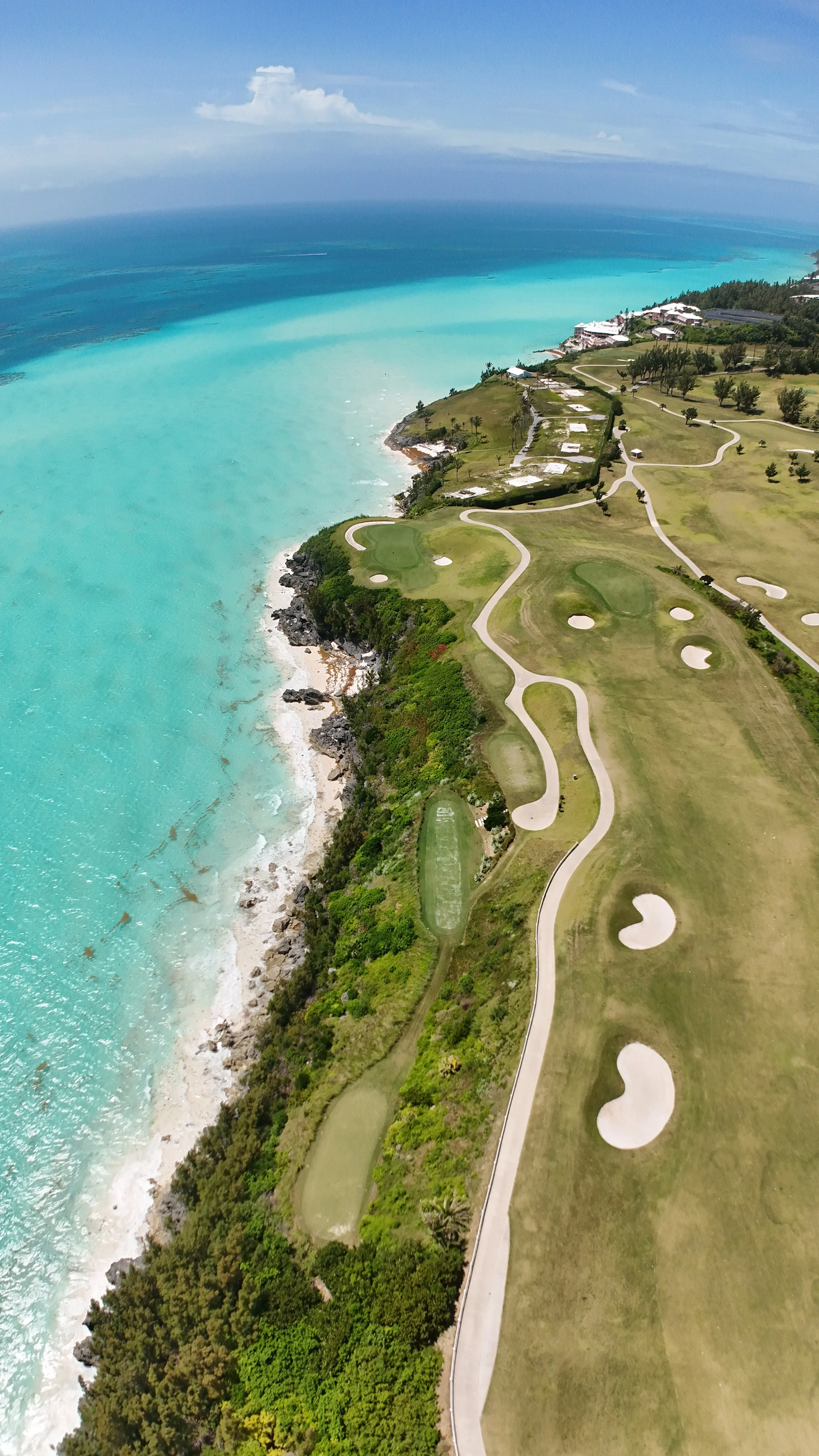 Aerial view of a golf course along the coastline with turquoise ocean water and sandy beaches, dotted with sand traps and pathways.