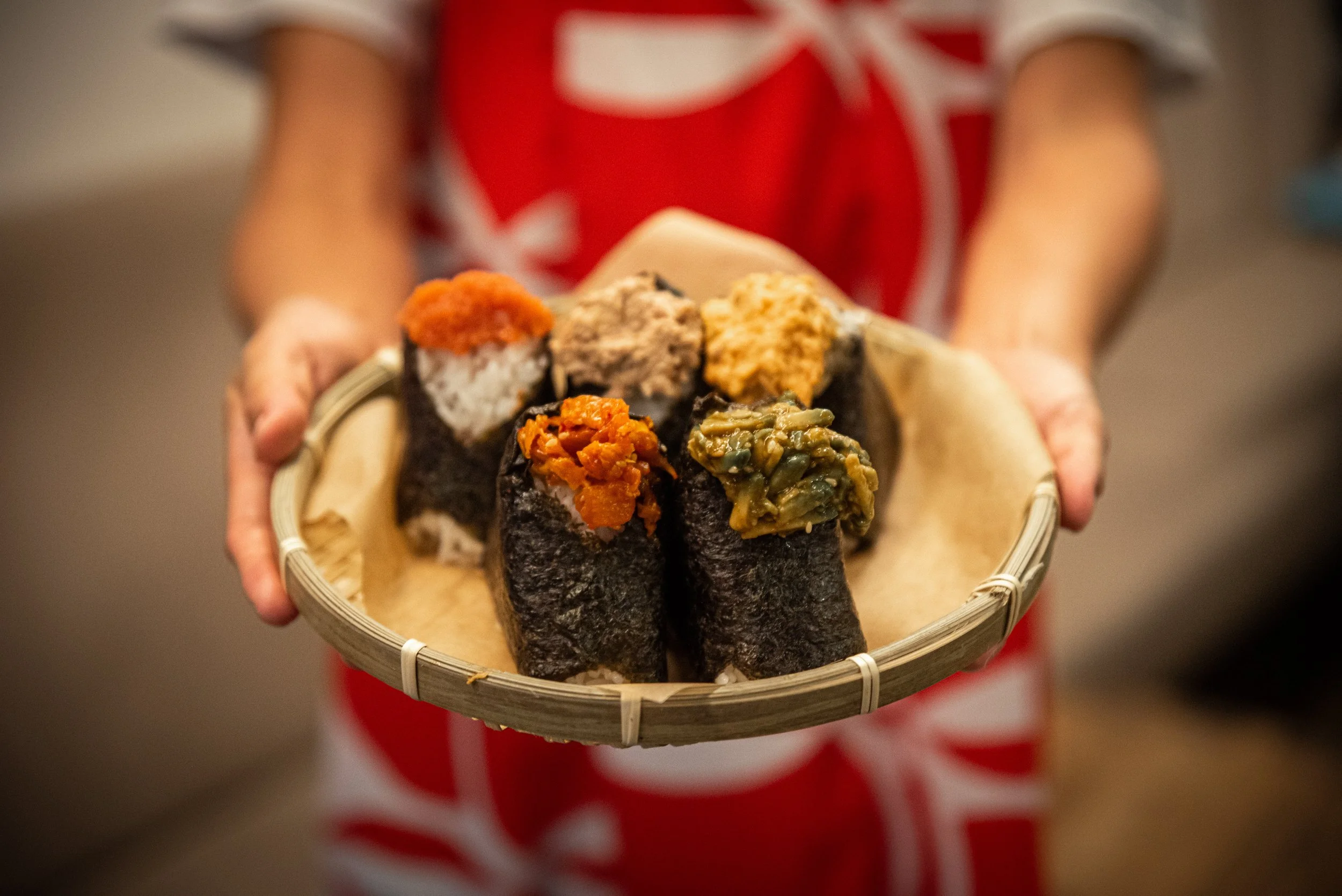 A person holding a bamboo tray of assorted sushi rolls with different toppings and fillings.
