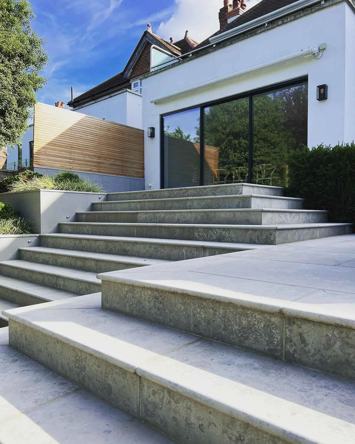 Modern house exterior with large glass sliding door, stone steps, and landscaped garden.