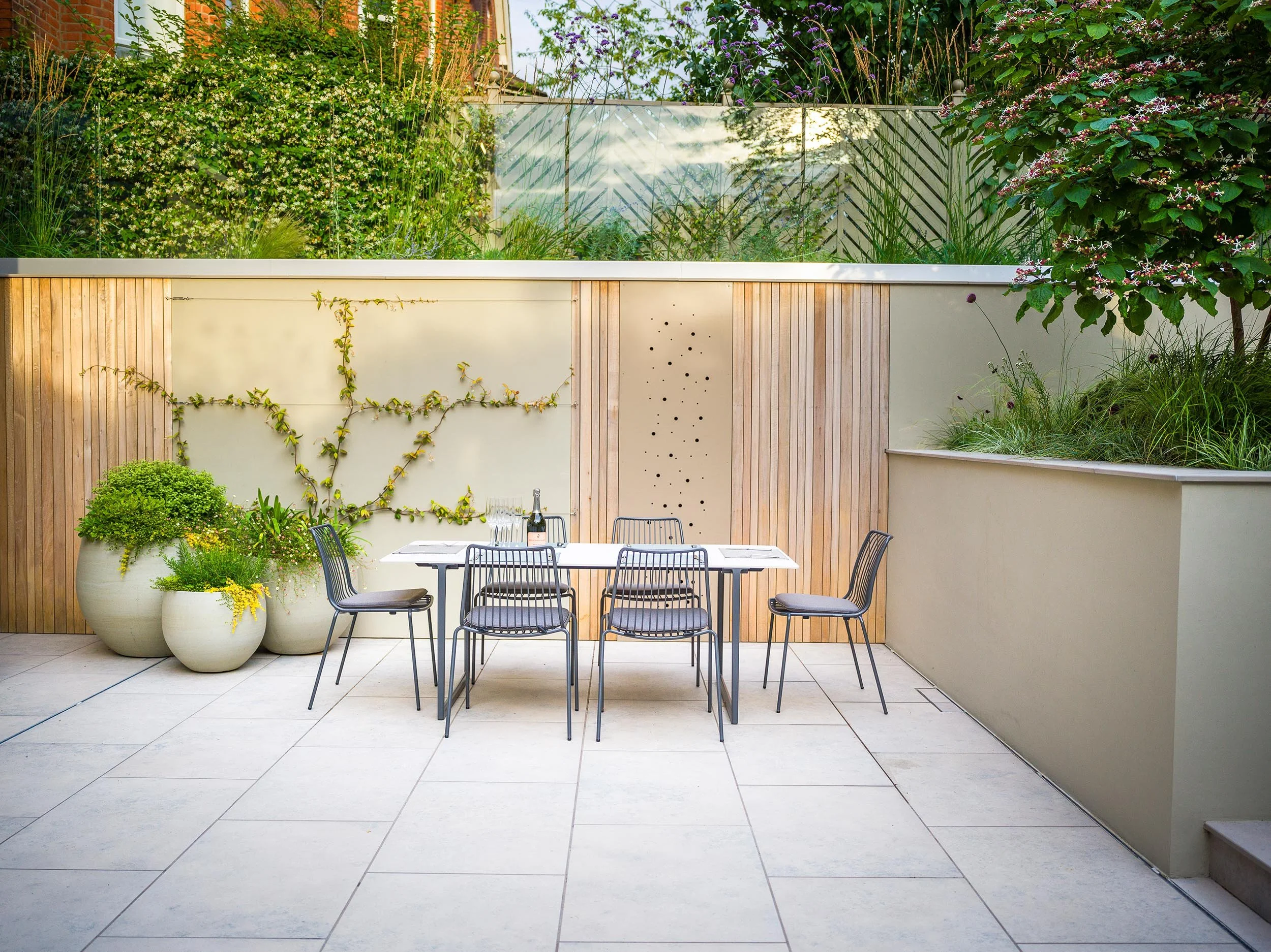 Outdoor dining area with black table and chairs against a cream wall with a decorative timber panel