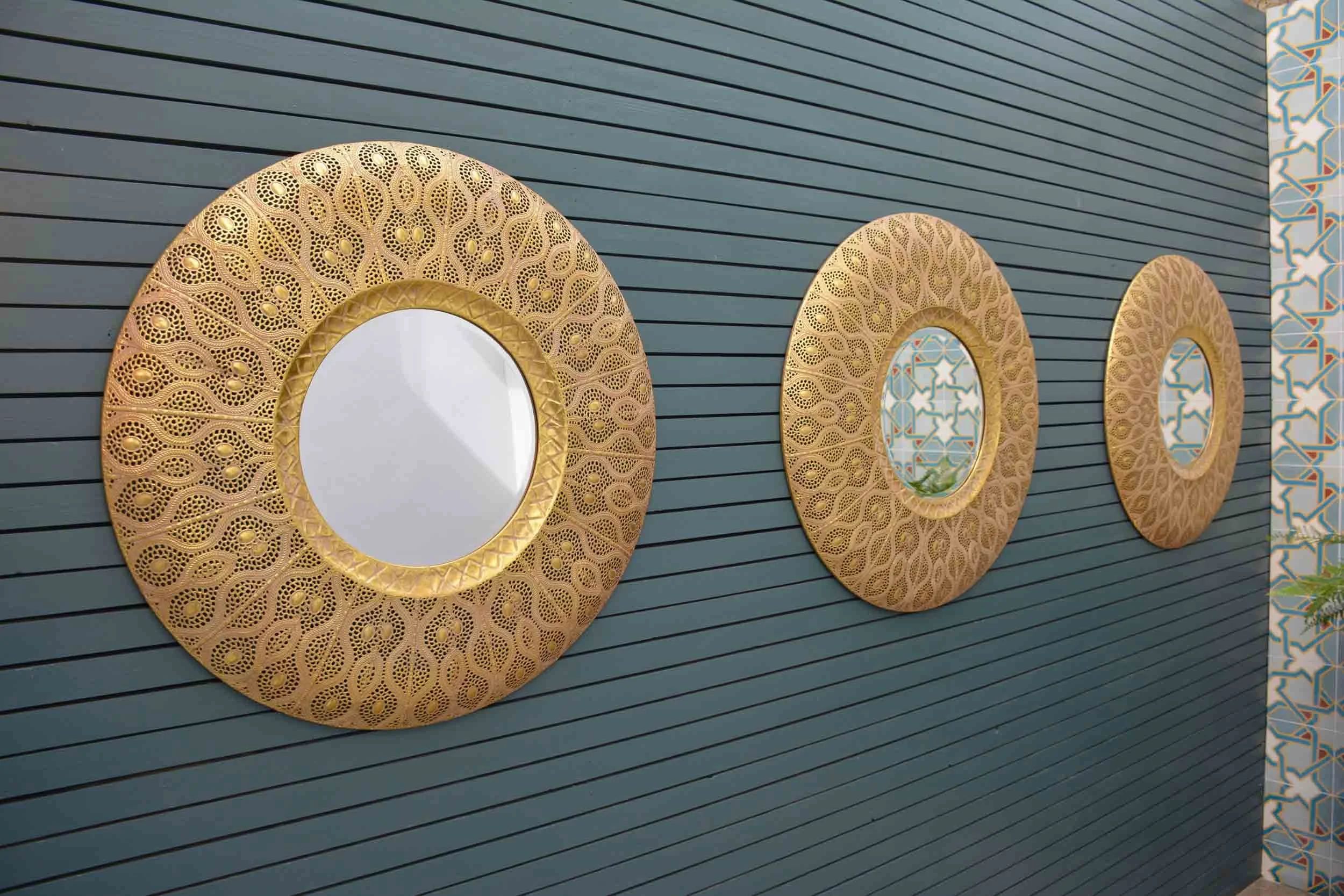 Three decorative gold circular mirrors with intricate patterns on a dark gray horizontal panel wall.