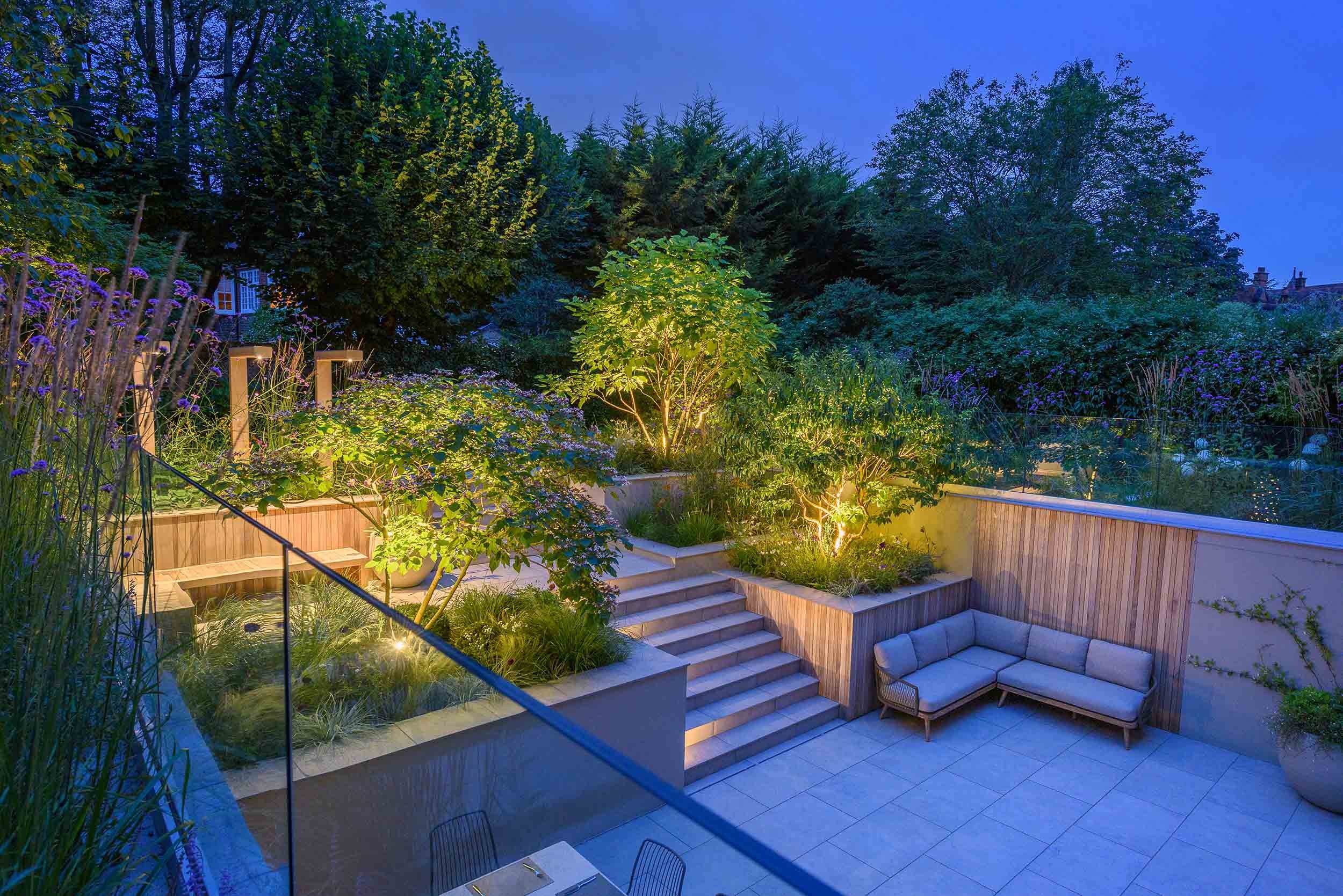 High angle view of a contemporary tiered garden at night with illuminated trees and warm lighting on the stone steps