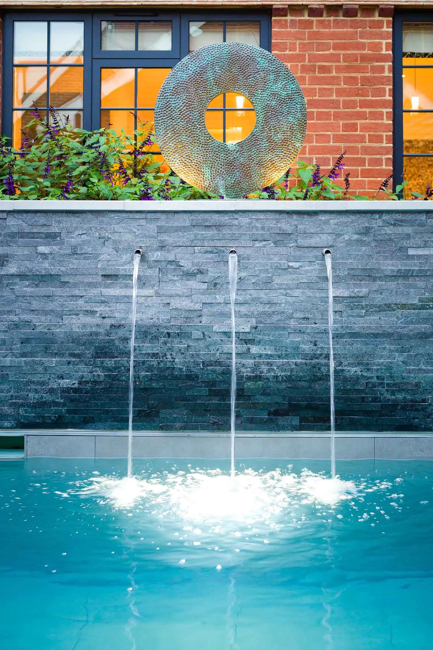 Circular garden water feature set into a brick wall with subtle lighting