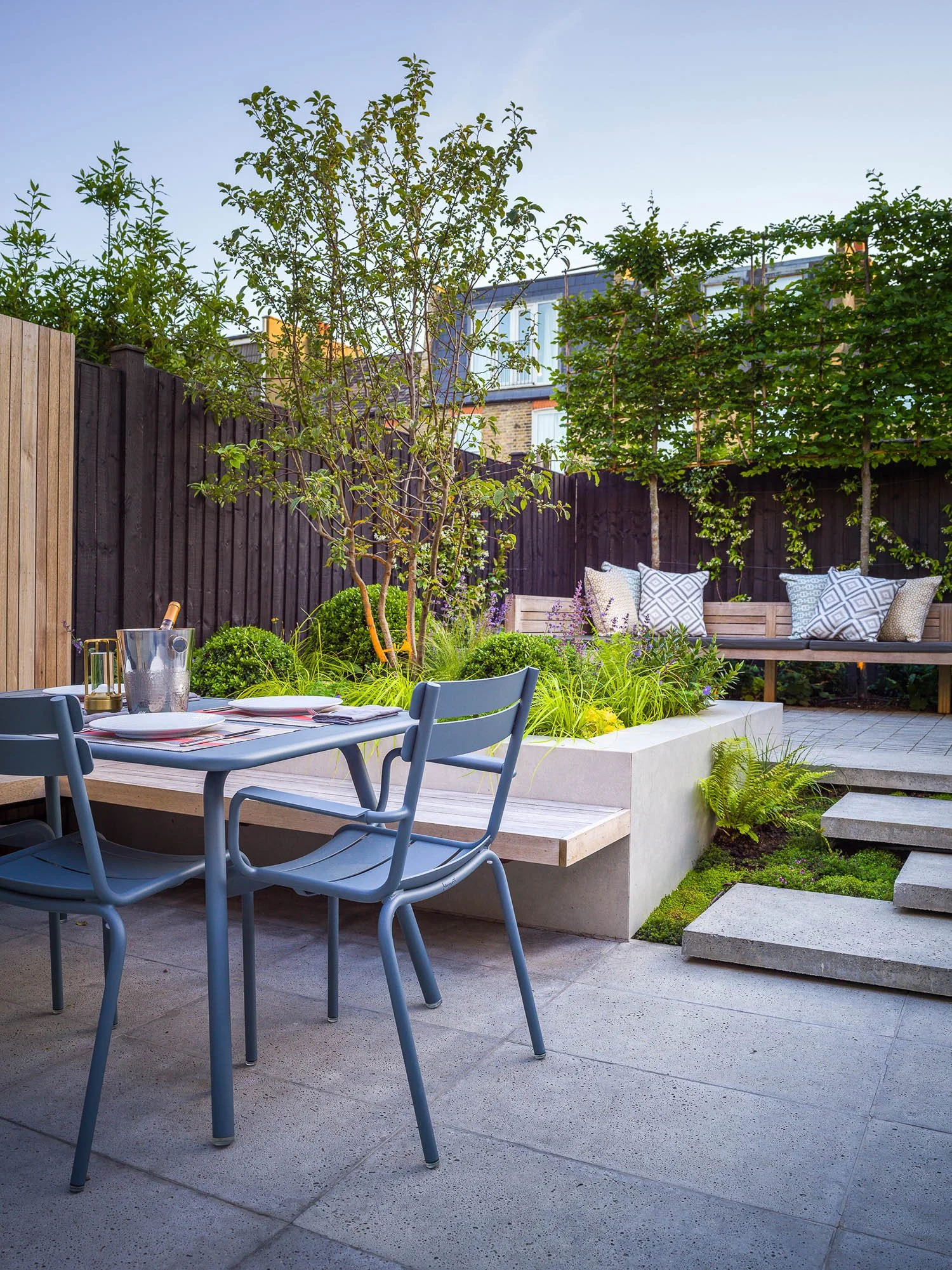 Evening view of the garden patio with the dining set and a lounge area, illuminated by soft garden lighting