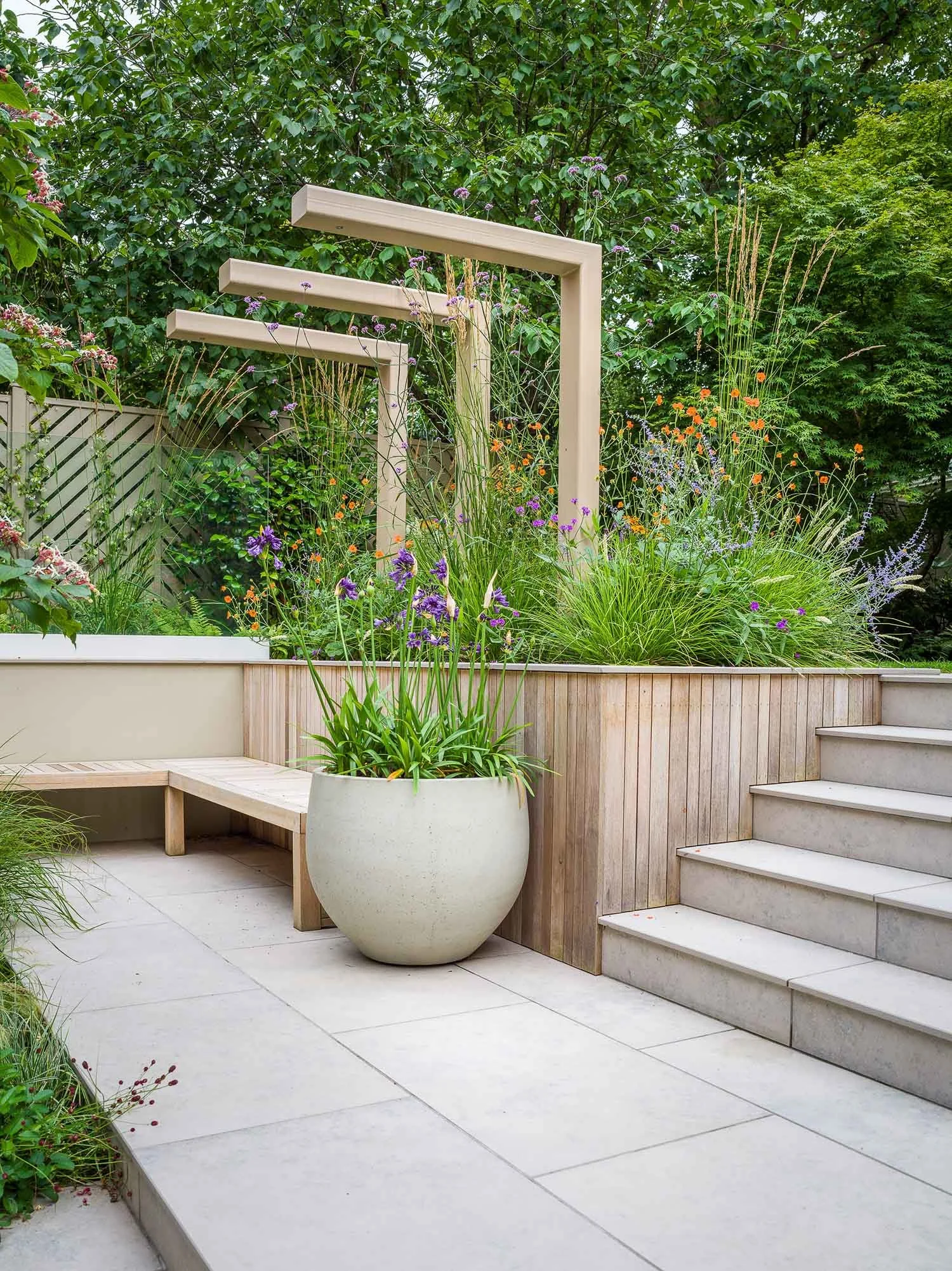 Modern timber pergola over a raised planter bed next to stone steps and a large spherical pot