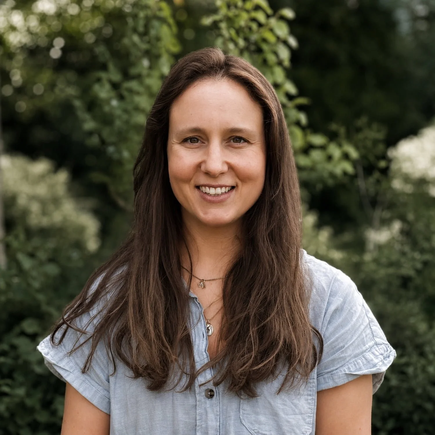 Sara from the garden design team smiling in a red top and traditional beaded necklace with blurred green trees behind