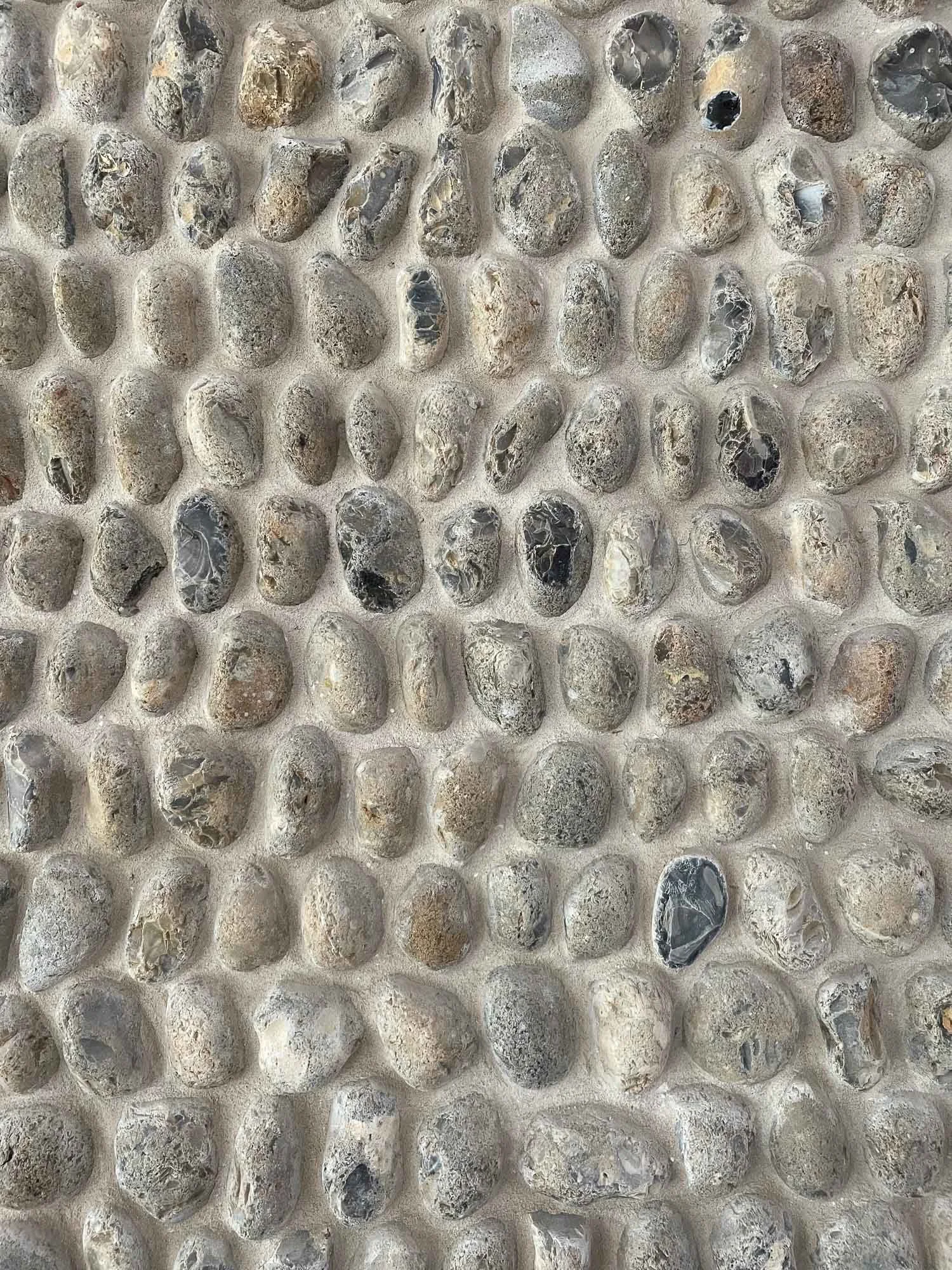 Close-up of a wall made of small, smooth, rounded stones embedded in light-colored cement.
