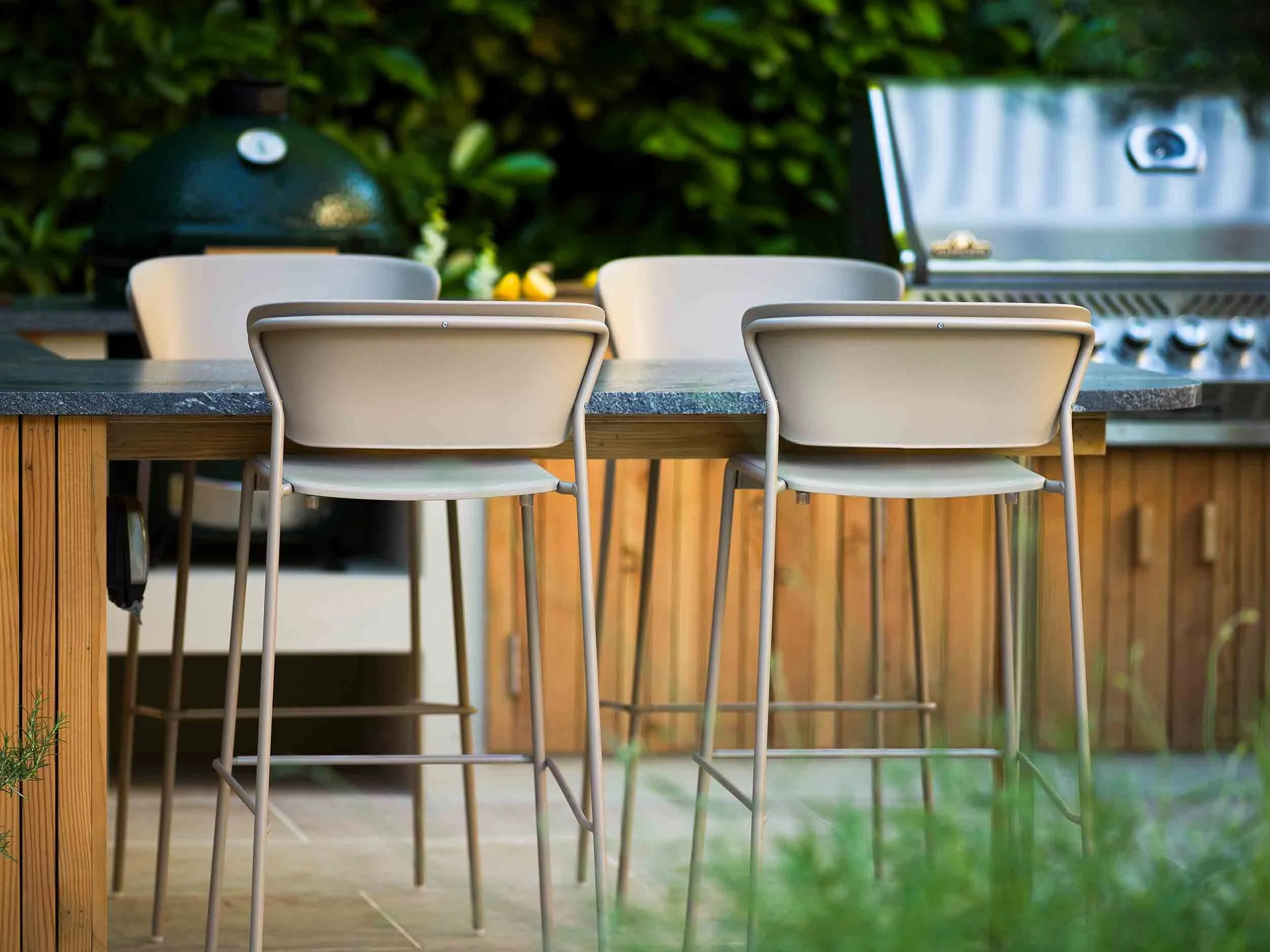 Modern grey bar stools at a stone outdoor kitchen counter with a Big Green Egg barbecue and stainless steel grill
