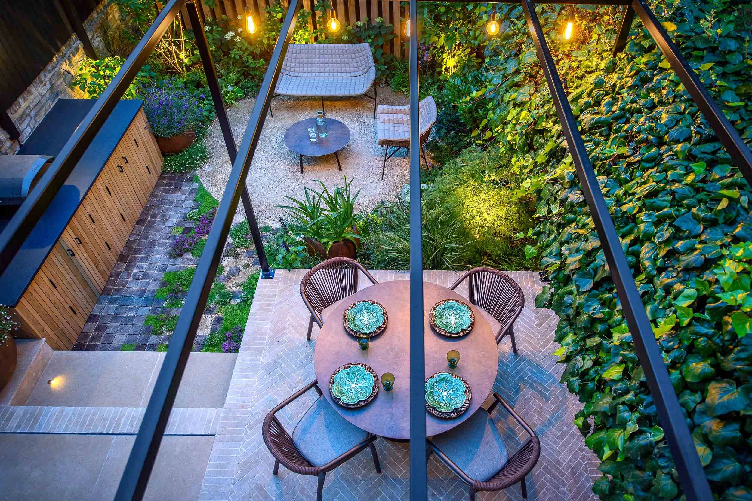 High angle view of a garden dining table set for a meal under a metal pergola with festoon lights
