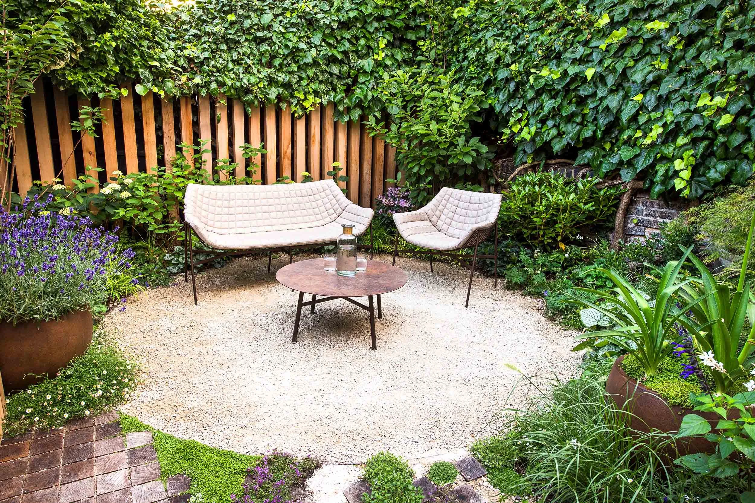 Gravel seating area with quilted outdoor chairs and a rusty metal table in a garden with lavender and climbing ivy