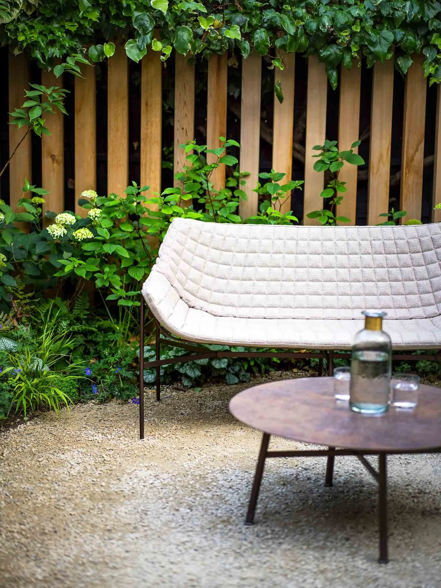 Modern beige quilted sofa set against a timber fence and green garden foliage