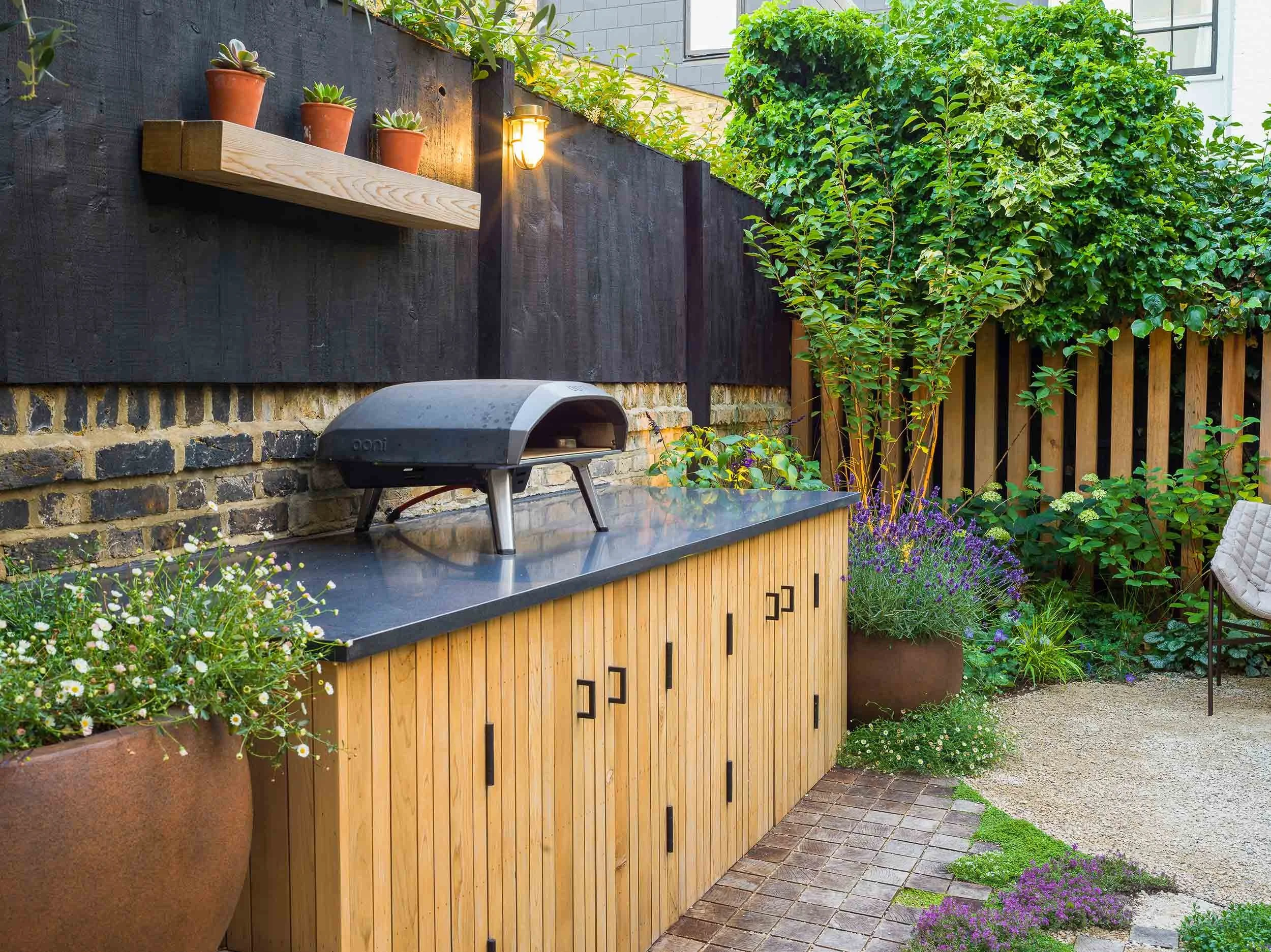 Outdoor kitchen area with a pizza oven on a wooden cabinet next to a large pot of lavender