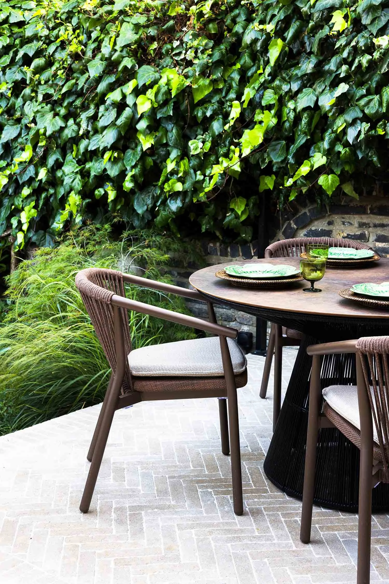 Contemporary brown garden chair with woven rope detail at a dining table beside green foliage