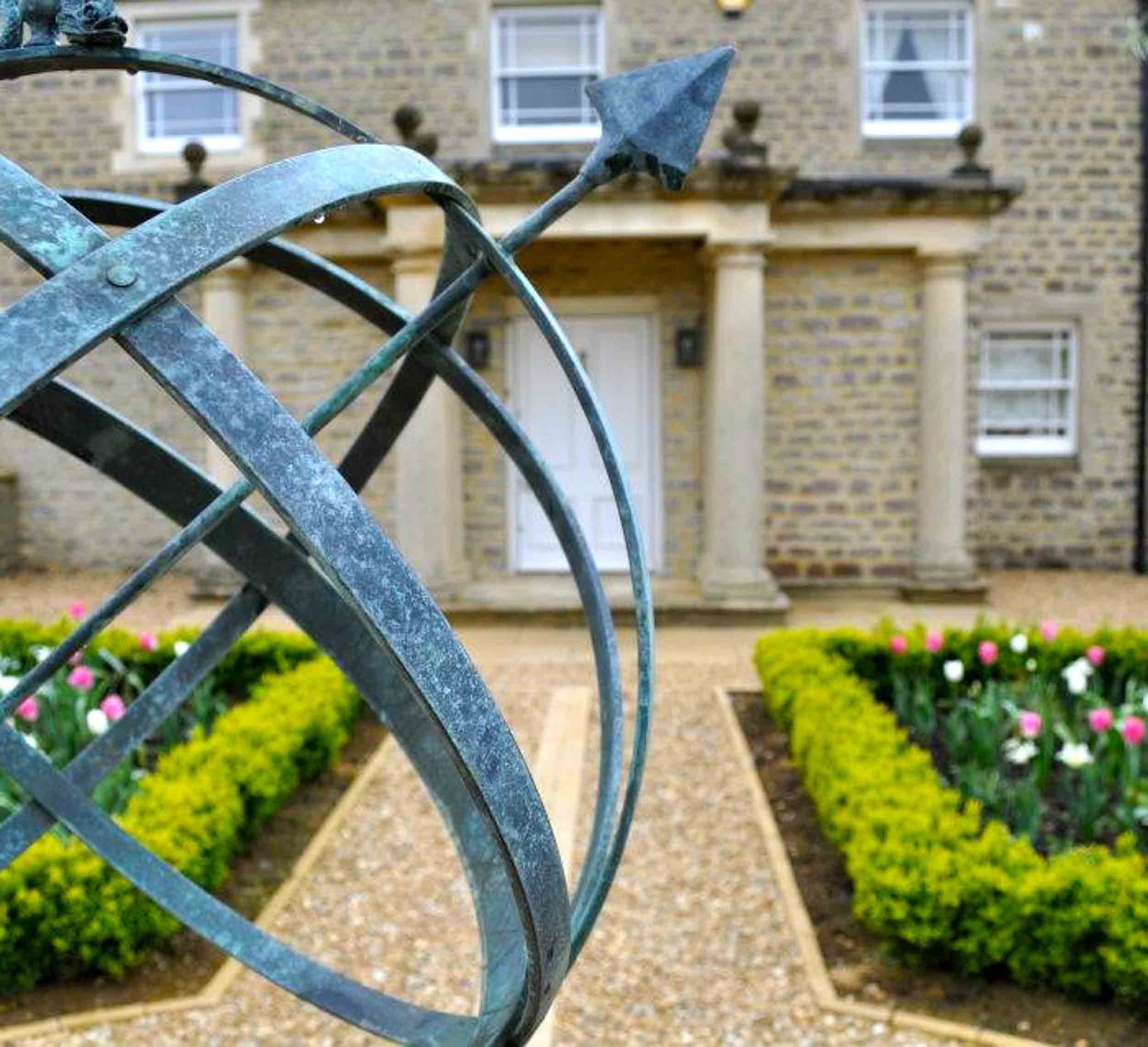 Close-up of an ornate metal gate with a house and garden in the background.