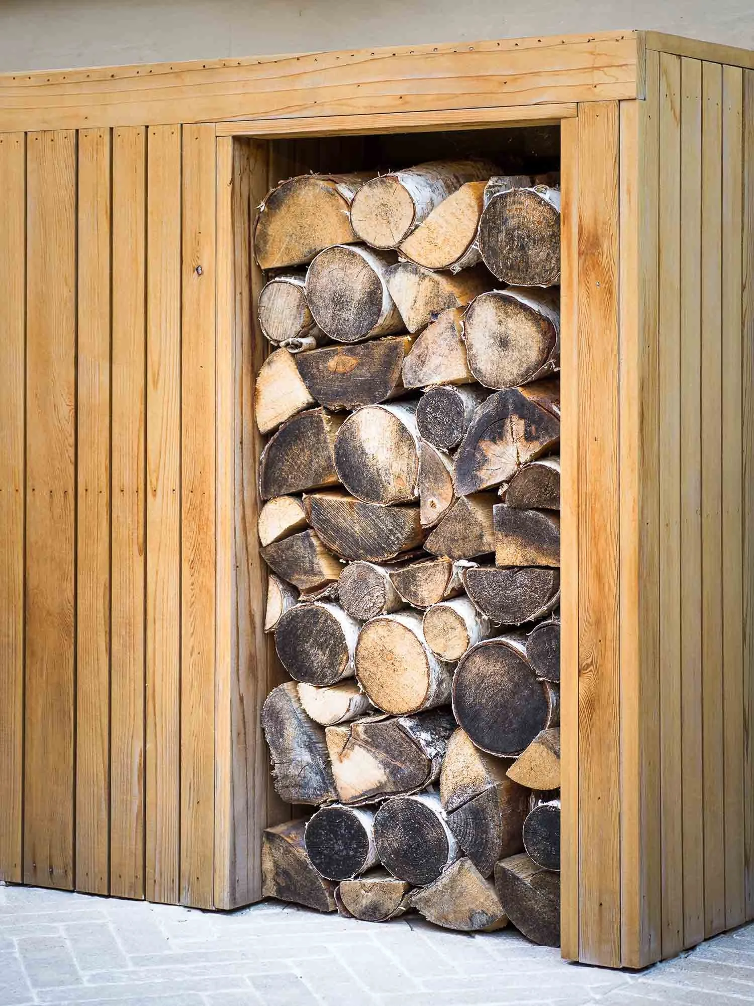 Neatly stacked firewood inside a tall custom built wooden storage unit in a garden setting