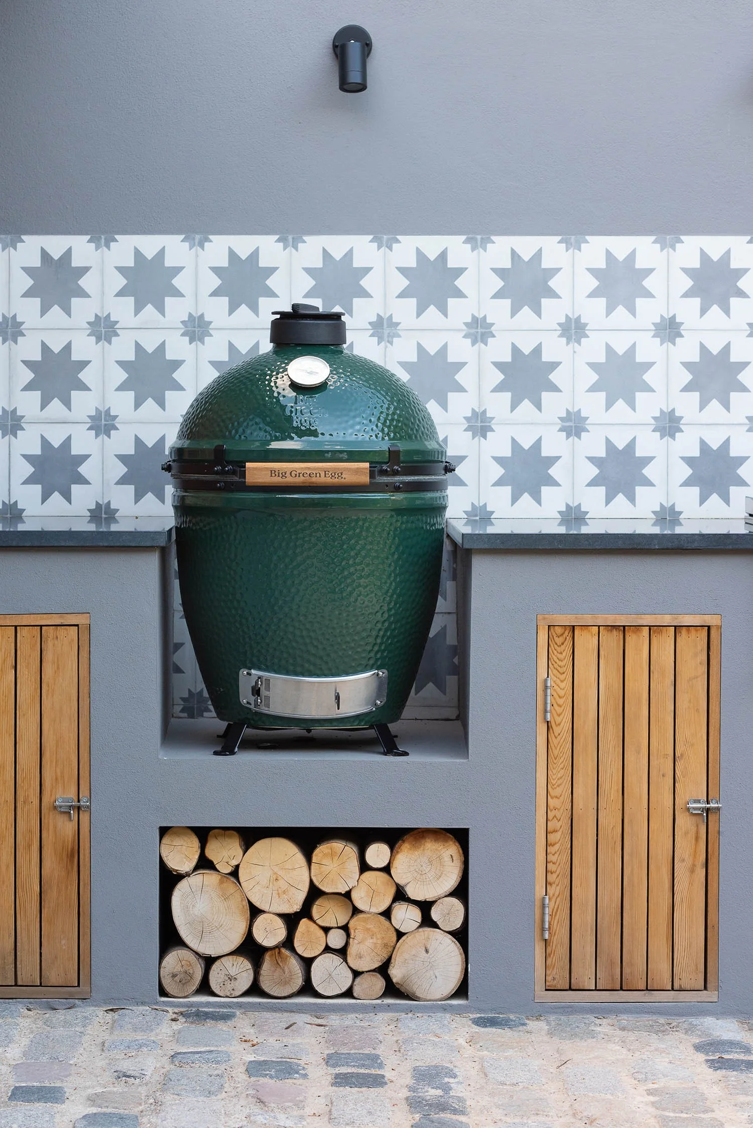 Large green ceramic outdoor oven built into a grey rendered wall with timber doors and star pattern splashback