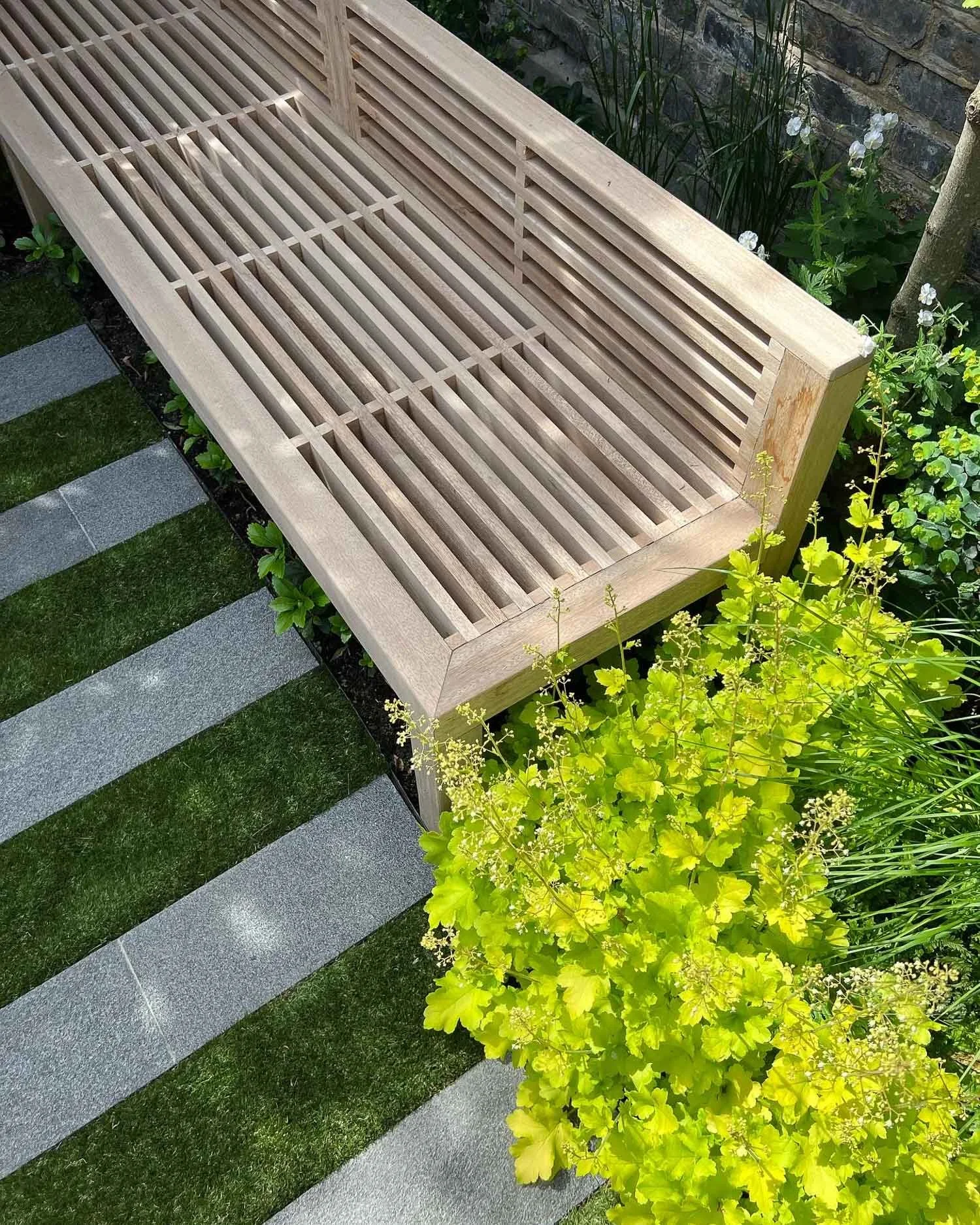 A wooden outdoor bench with slatted design in a garden surrounded by plants and greenery.