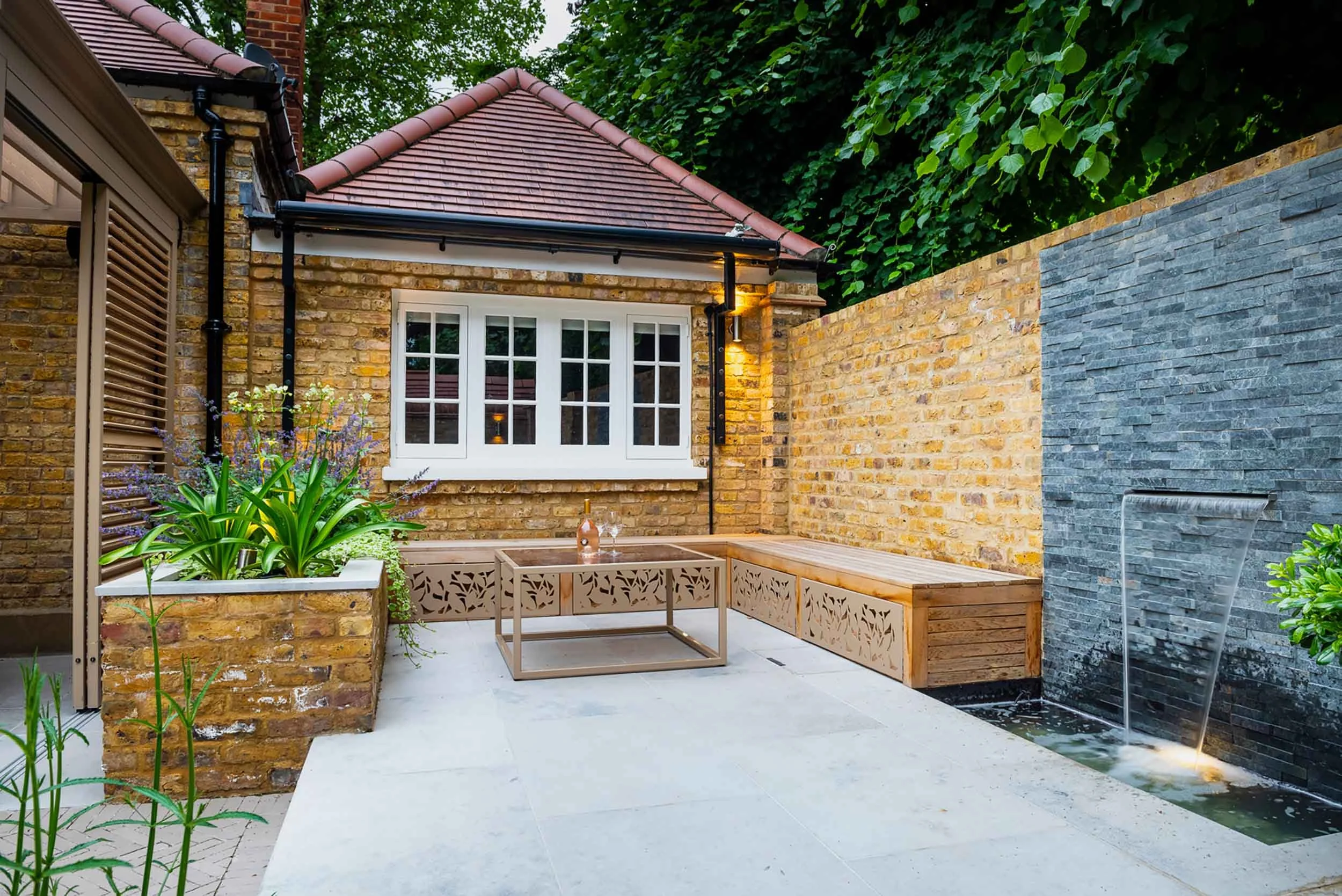 Integrated garden seating with decorative laser cut panels next to a slate water feature and raised brick planter