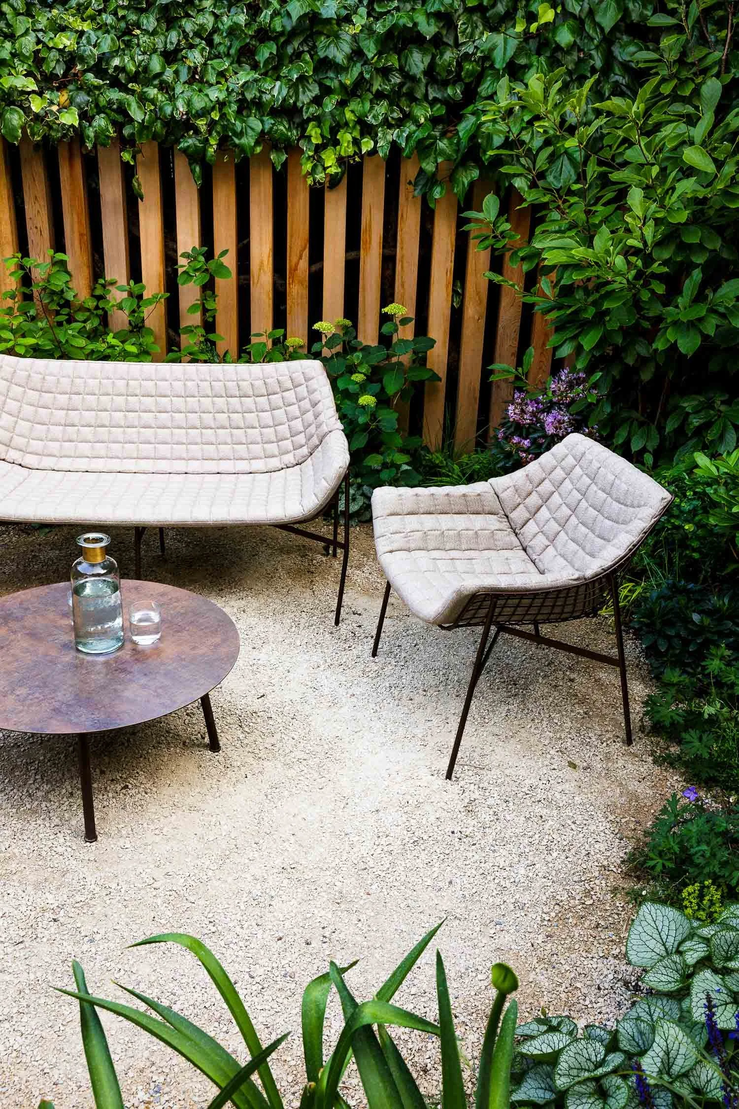 Close up of a modern quilted outdoor chair and round metal table on a light gravel surface