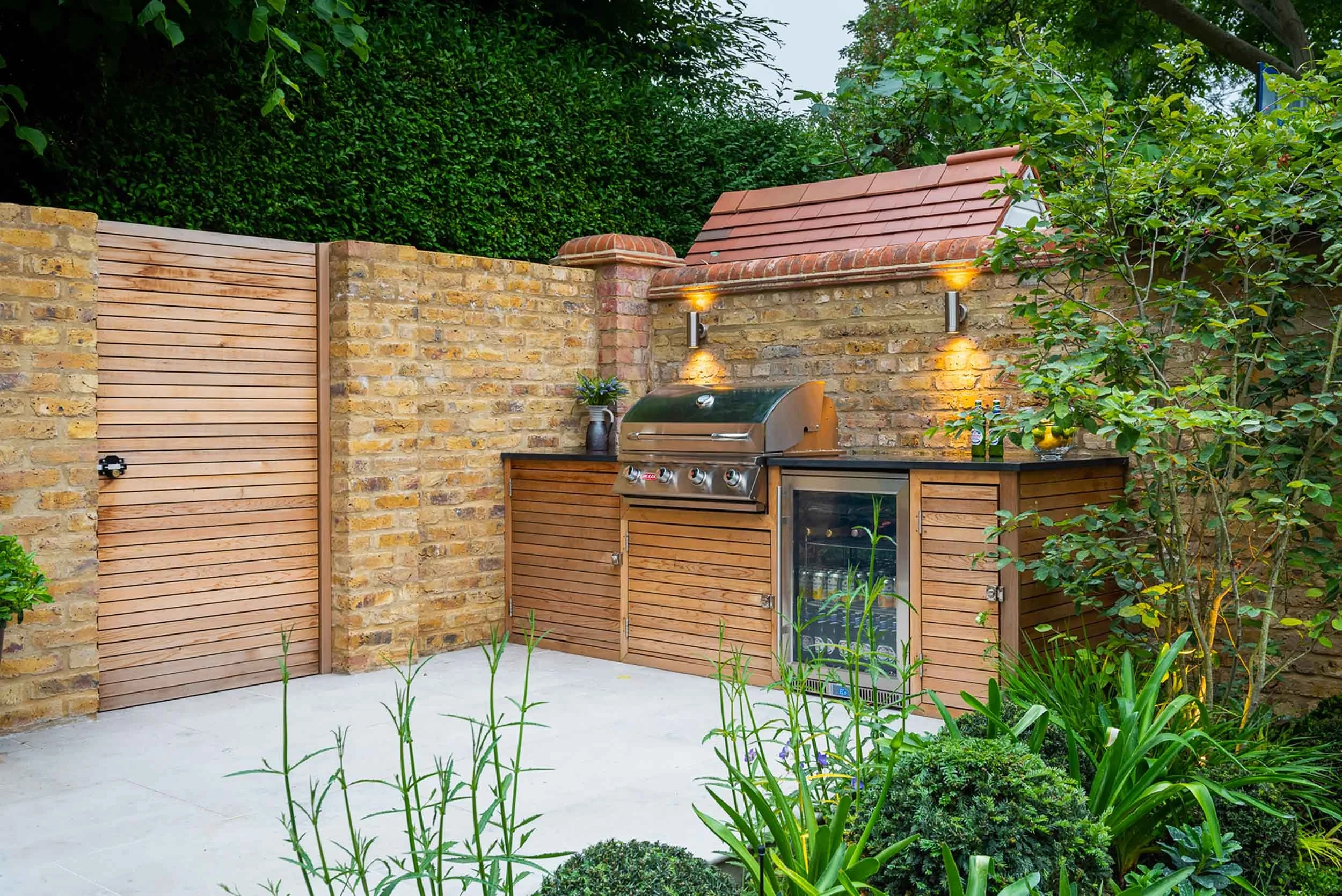 Garden patio with timber slatted gate outdoor kitchen and barbecue area with spotlights mounted on a yellow brick wall