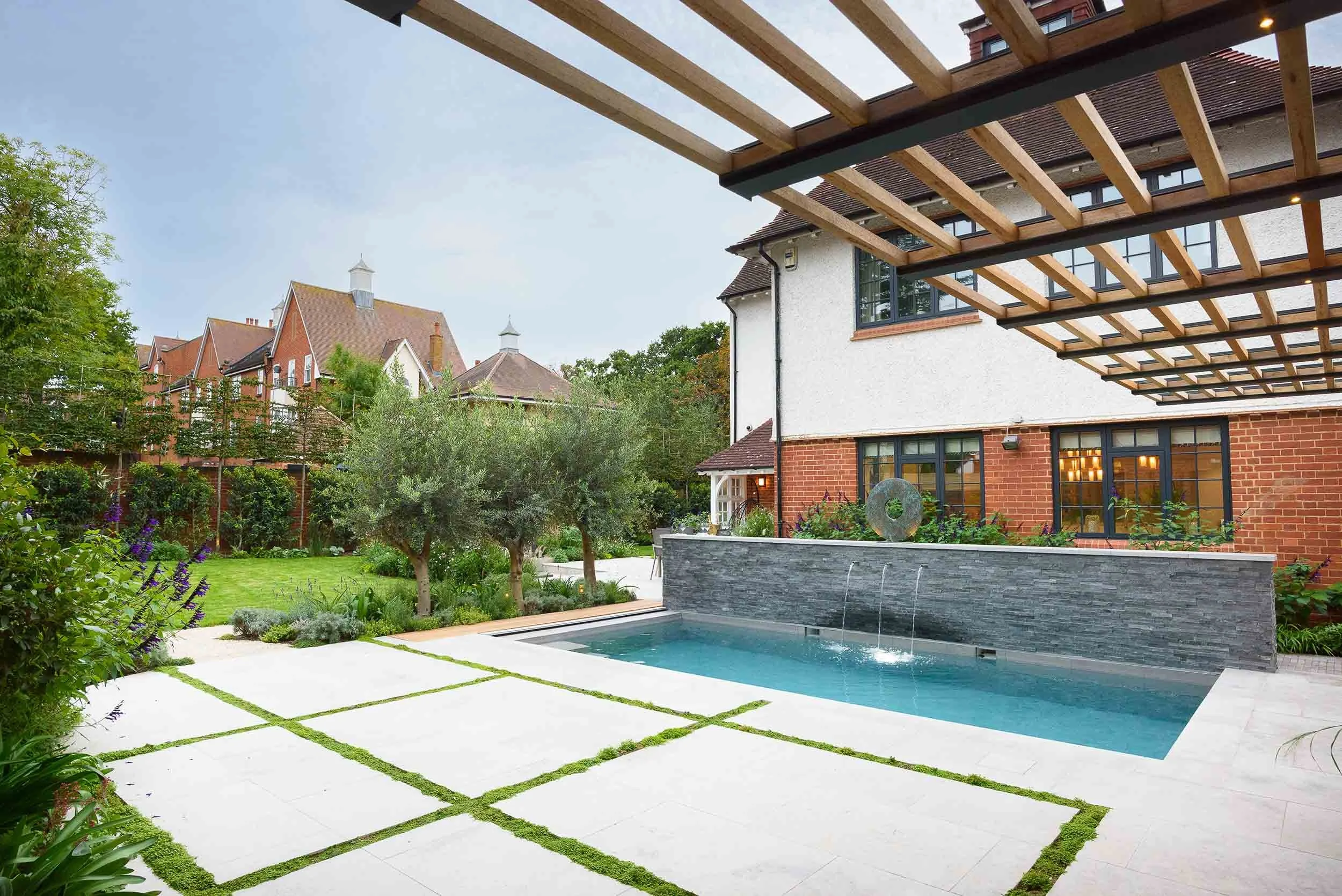 Pergola-covered terrace beside swimming pool with garden planting and seating