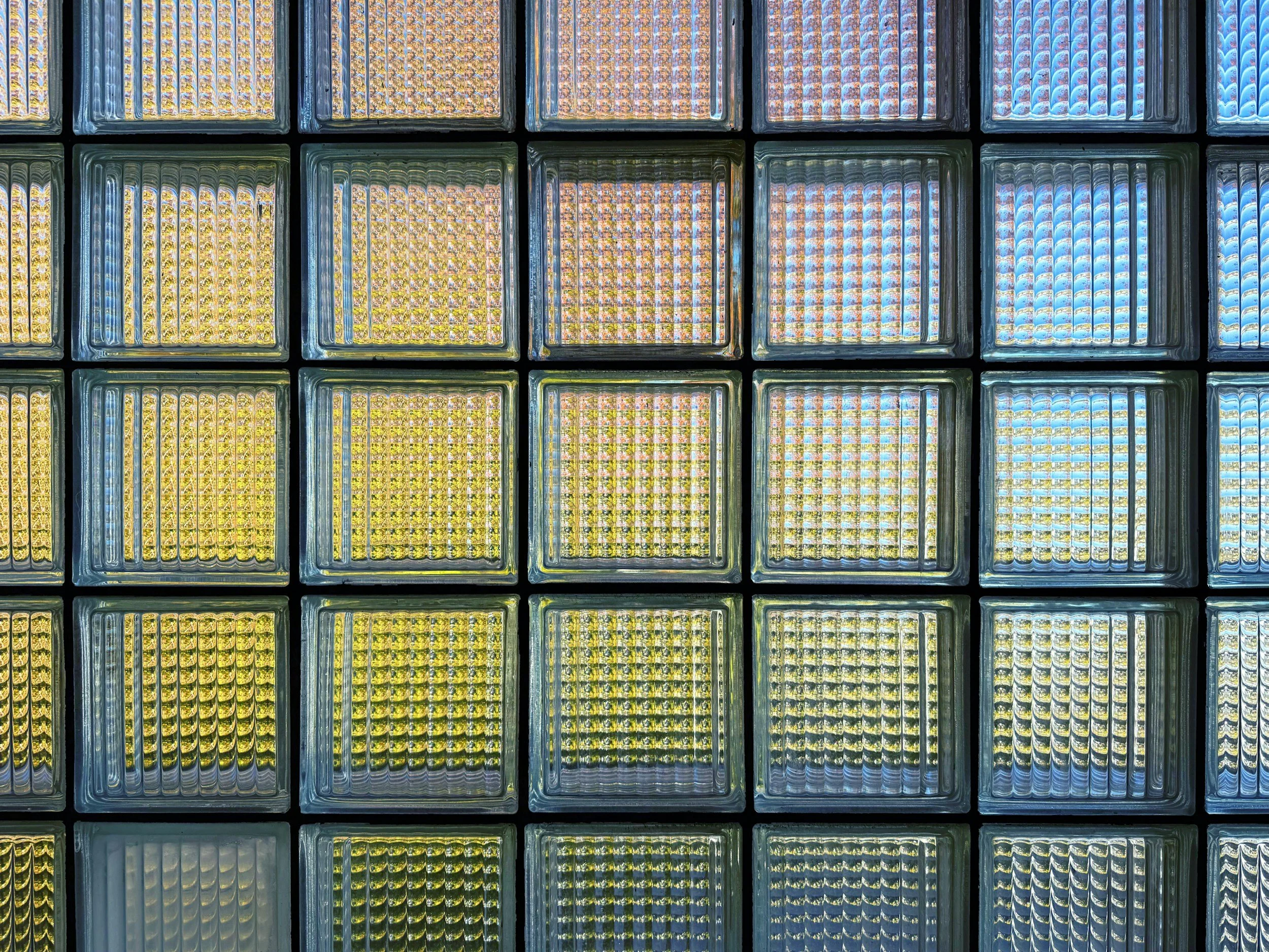 Close-up view of a wall made of glass blocks in Glasgow with colored lights illuminating from behind, creating a vibrant and textured pattern.