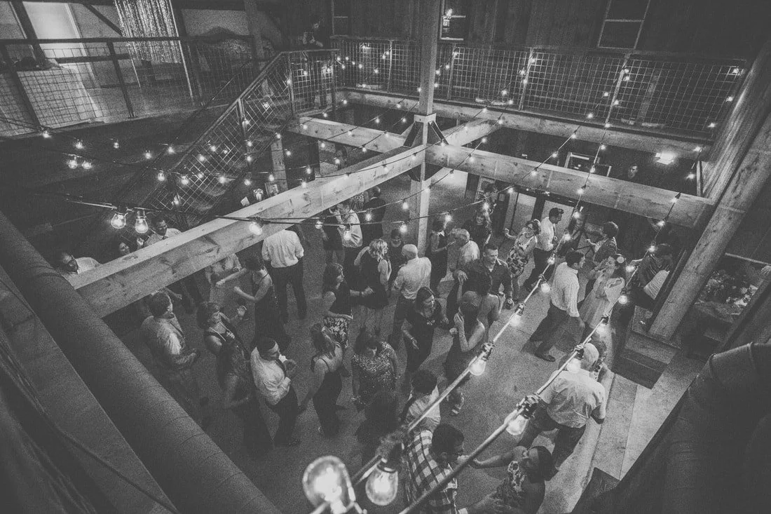 People dancing and socializing at an indoor party with string lights and industrial-style decor, viewed from above.