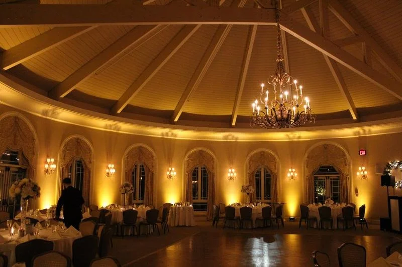 Elegant banquet hall with a high vaulted ceiling, chandelier, and lit wall sconces. Round tables with floral centerpieces are set for a formal event.