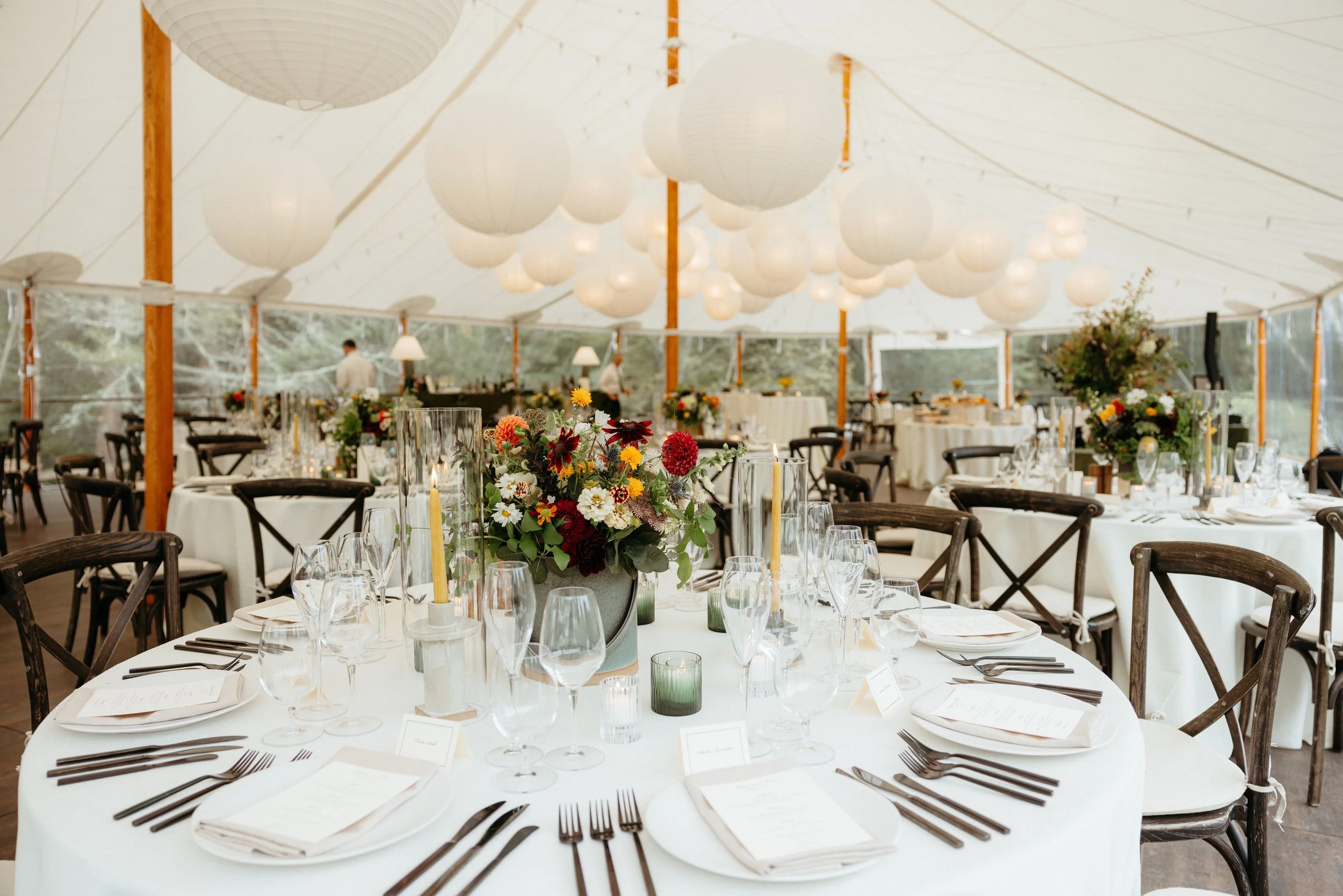 Elegant event tent with round tables decorated with floral centerpieces, candles, and tableware for a formal occasion.