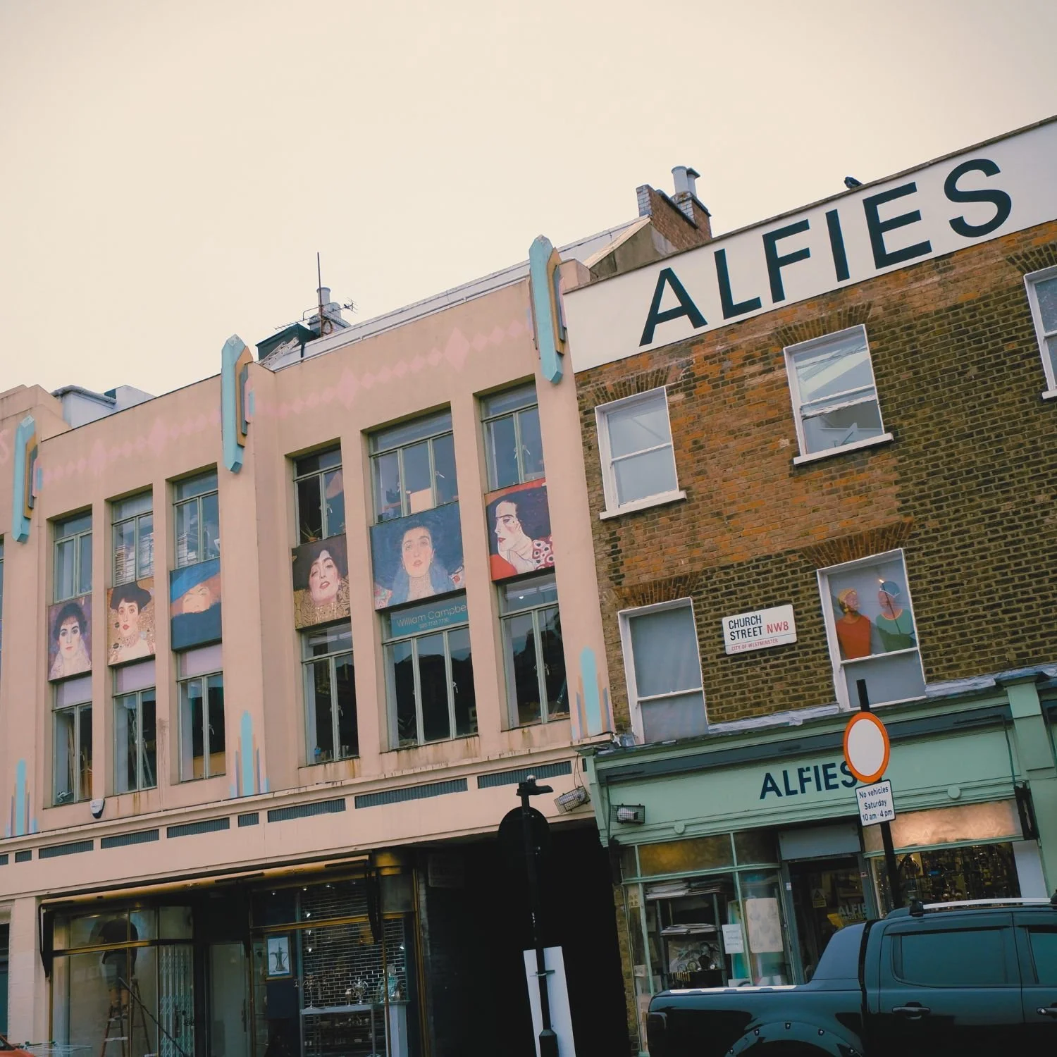 Exterior view of the Alfies building with artwork and windows, street sign, and parked vehicle in front.