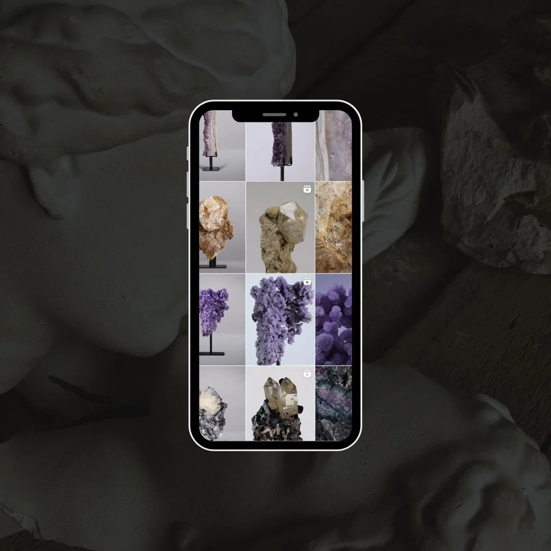 An iPhone displaying a photo gallery of different mineral and crystal specimens, including amethysts and other gemstones, against a background of artistic sculptures or busts.