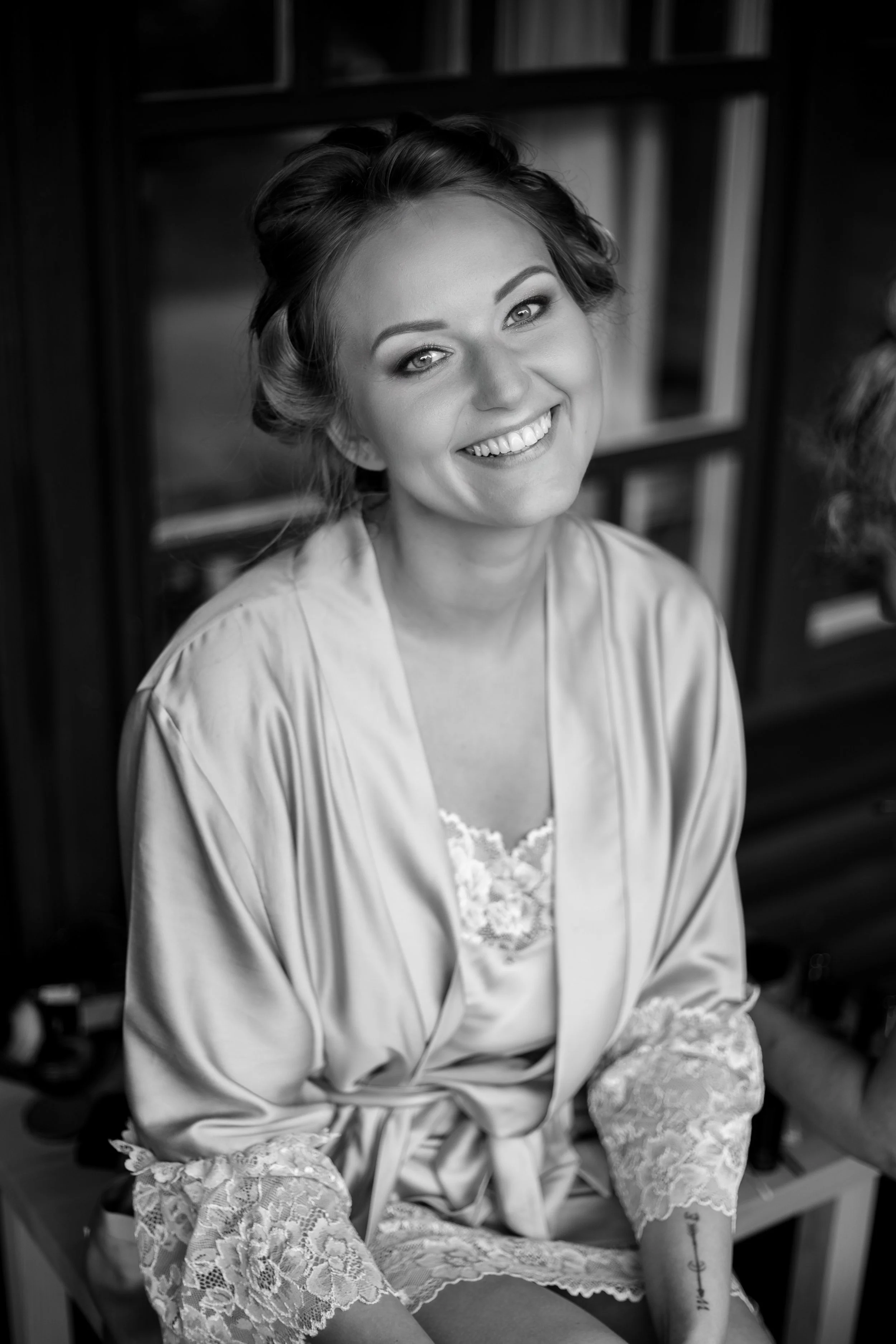 Black and white photo of a woman smiling, wearing a satin robe with lace cuffs.