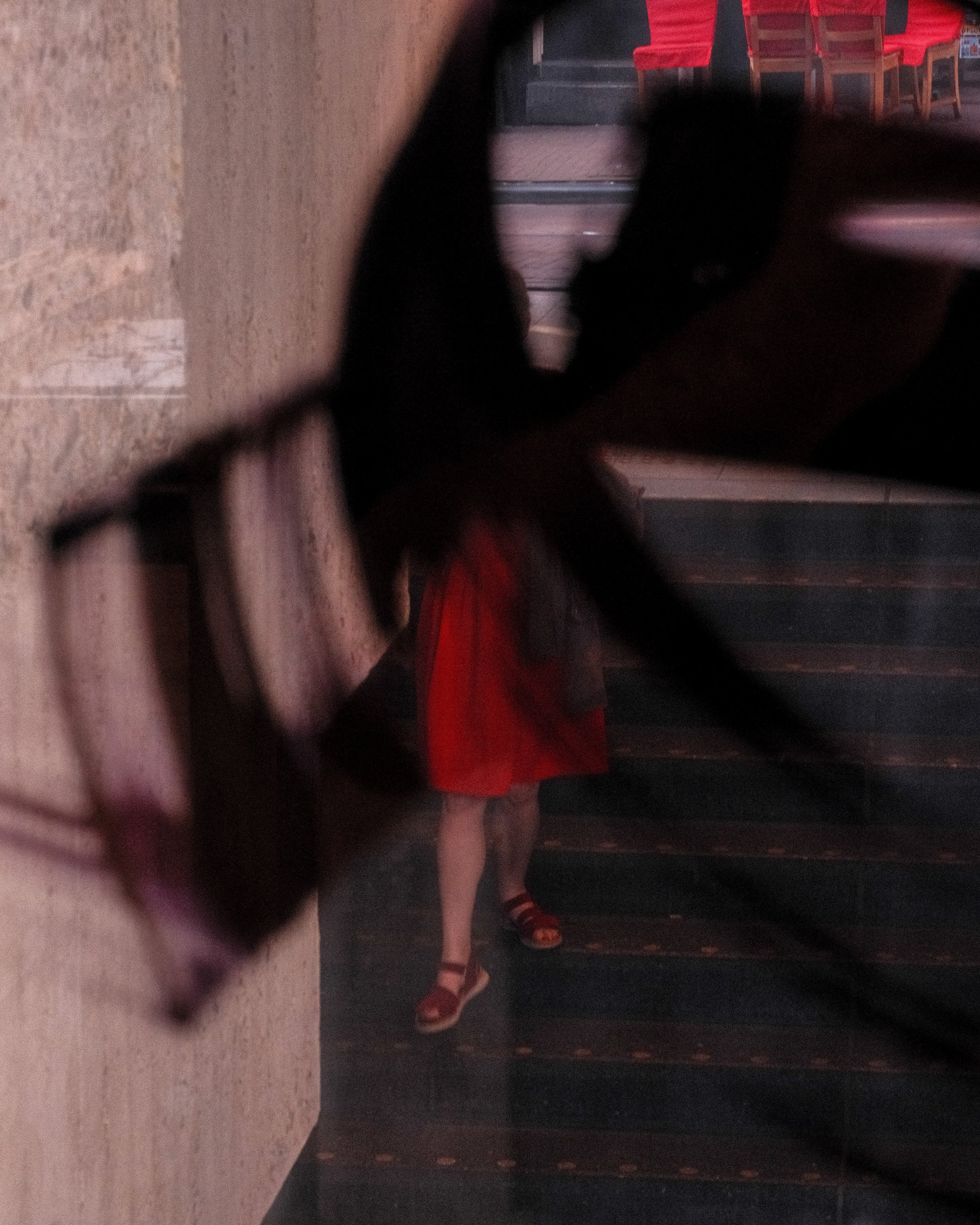 Photo of a person in a red dress and sandals, taken through an object in the foreground, with stairs and seats in the background.