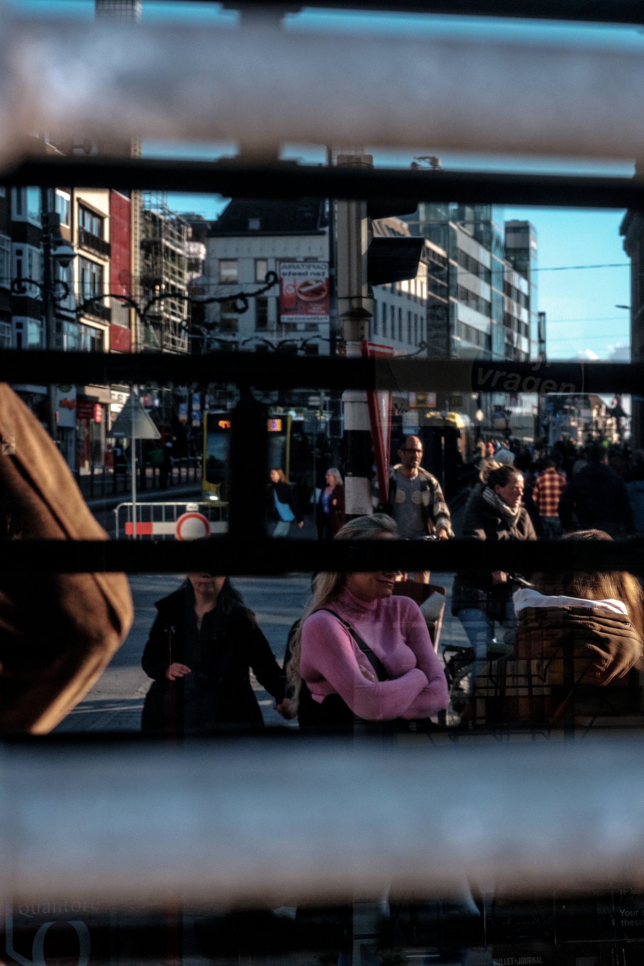 People walking and standing on a city street viewed through a window with horizontal bars.