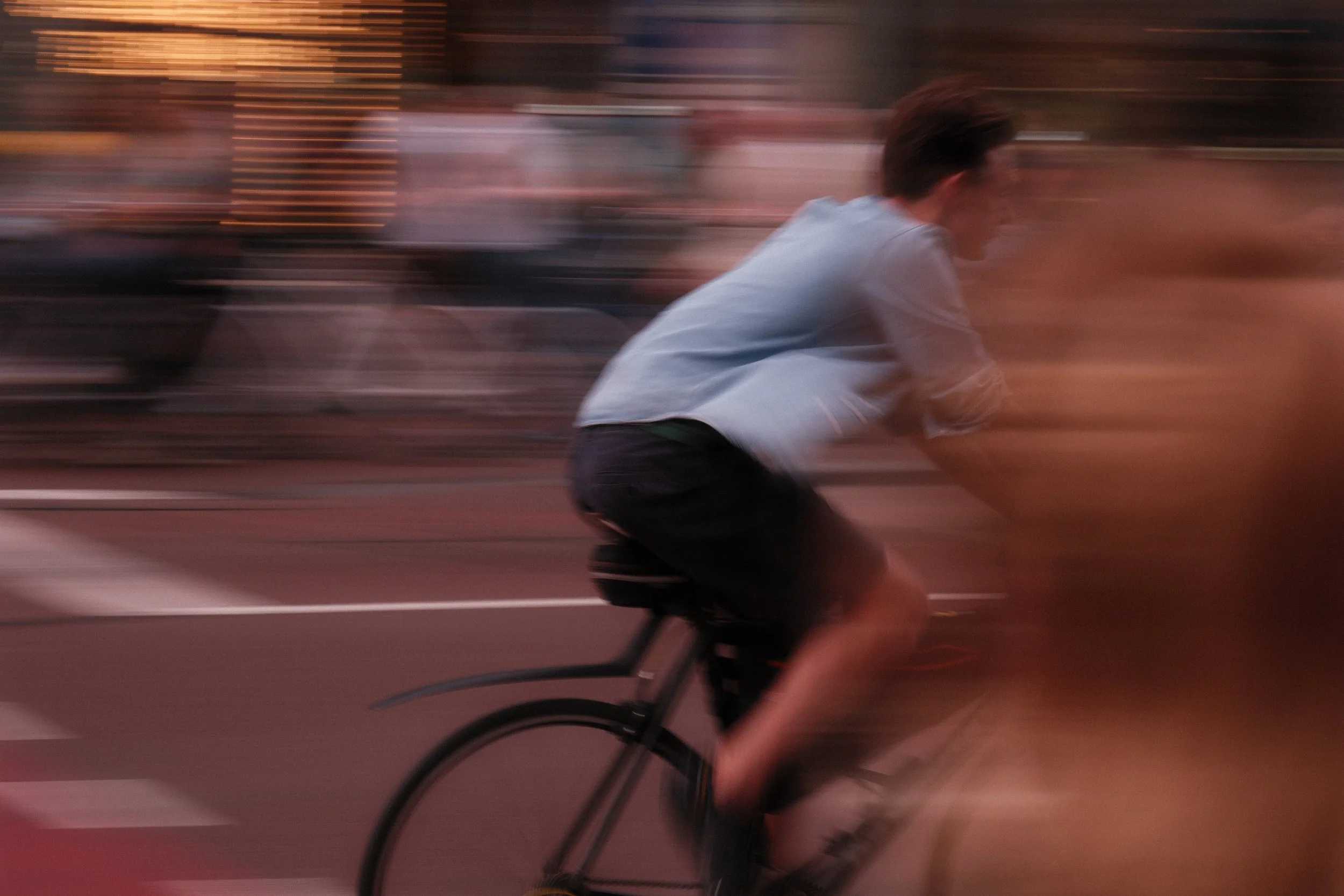 A person riding a bicycle at high speed on a city street during sunset, with a blurred background and motion blur.