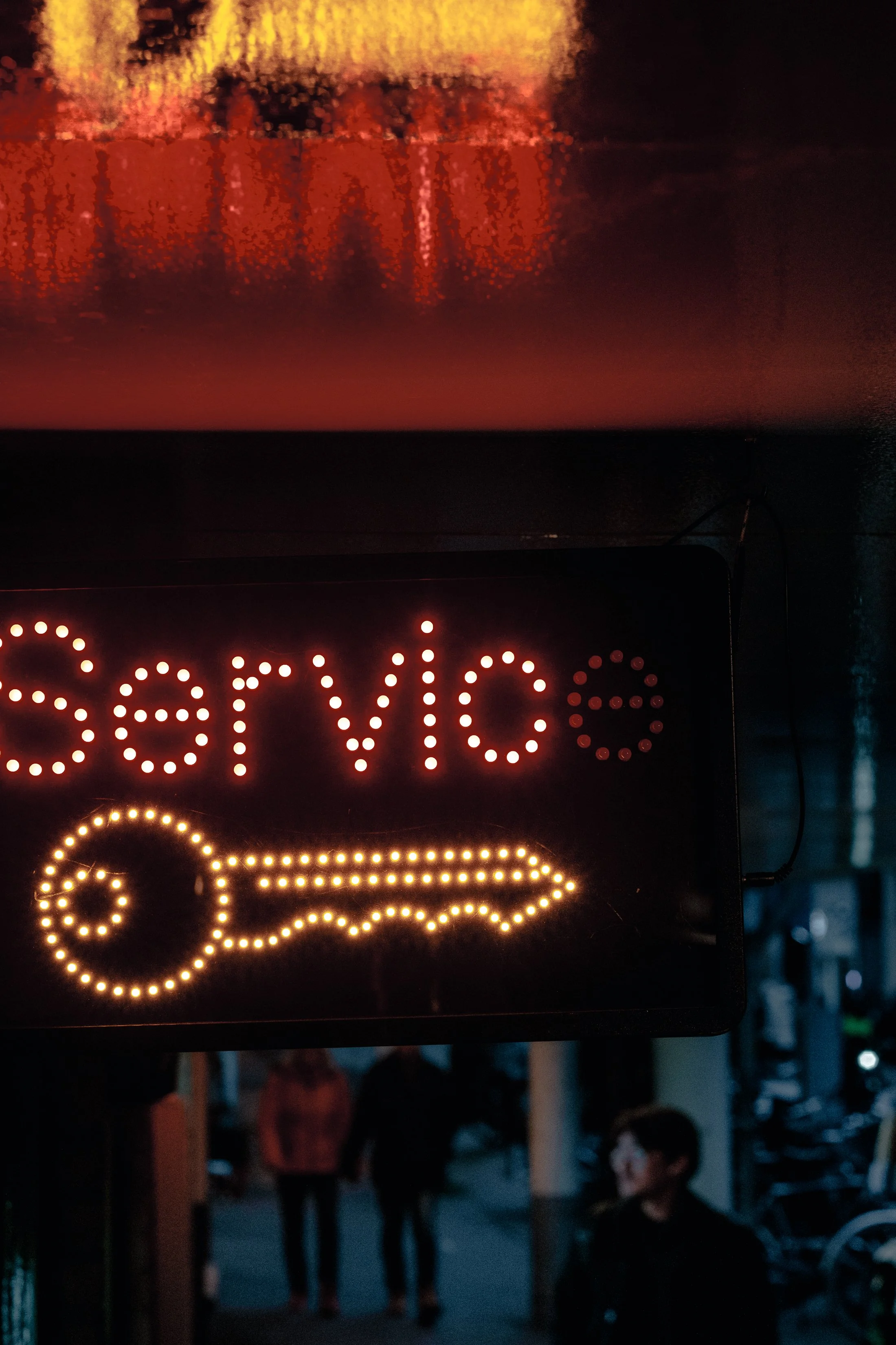 A neon sign with the word 'service' and a key symbol underneath, both made of small lights, located on the exterior of a building at night.