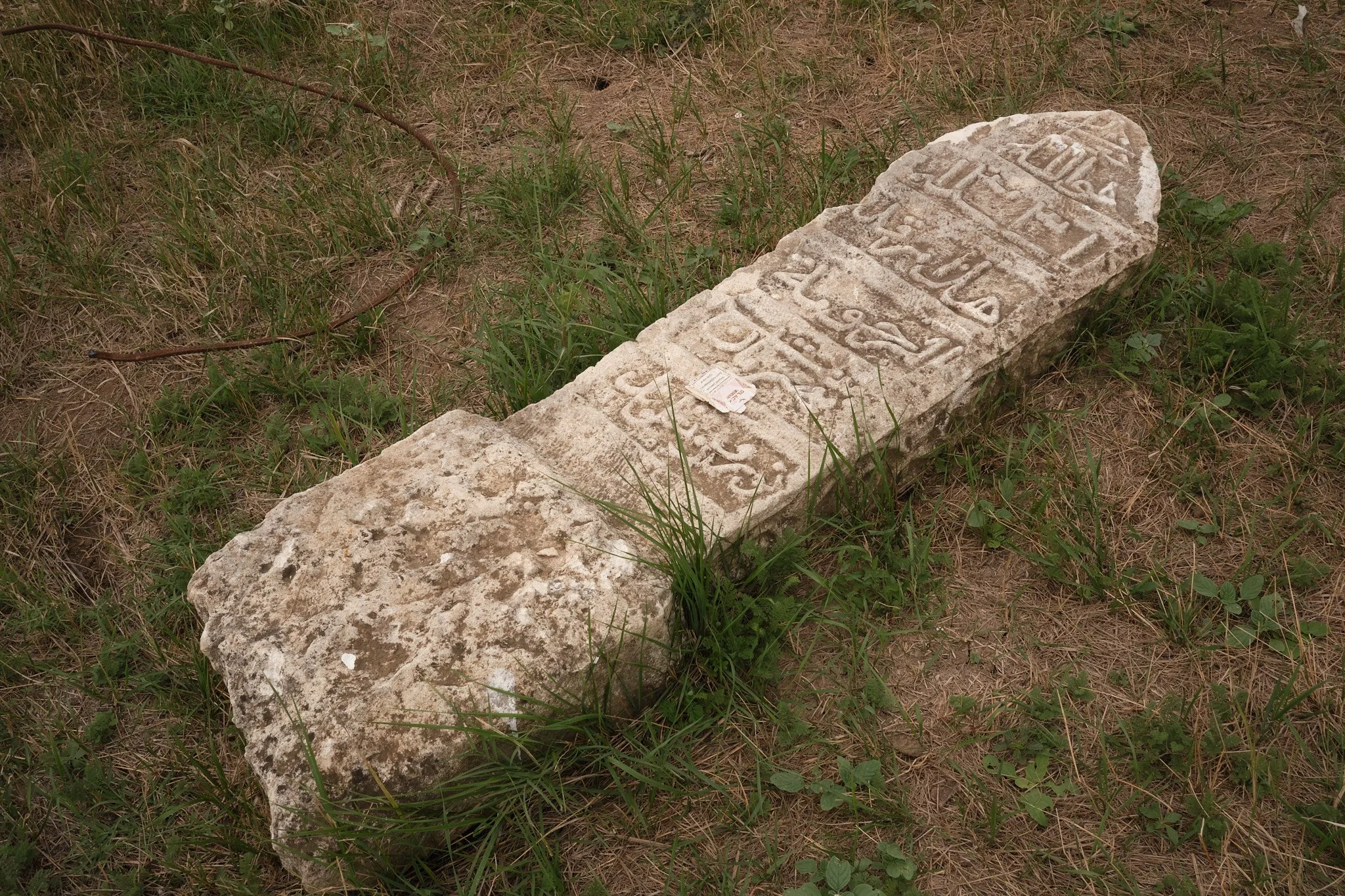 In a cemetery in Nagorno-Karabakh, a weathered headstone lies partly hidden in the grass with an empty cigarette box pressed onto it. Its inscription is carved in Arabic script, used here over centuries to write Persian, Arabic and Turkic. The stone 