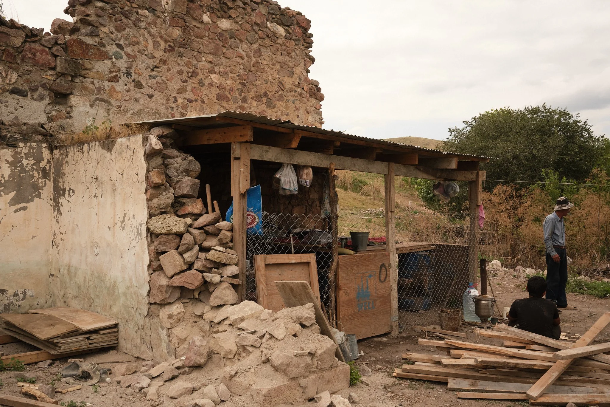 In what was previously the bathroom to a grander home in the village, a father and son now live inside, close enough to tend to their bees; Nagorno-Karabakh, in a village near Fuzuli, July 2026.