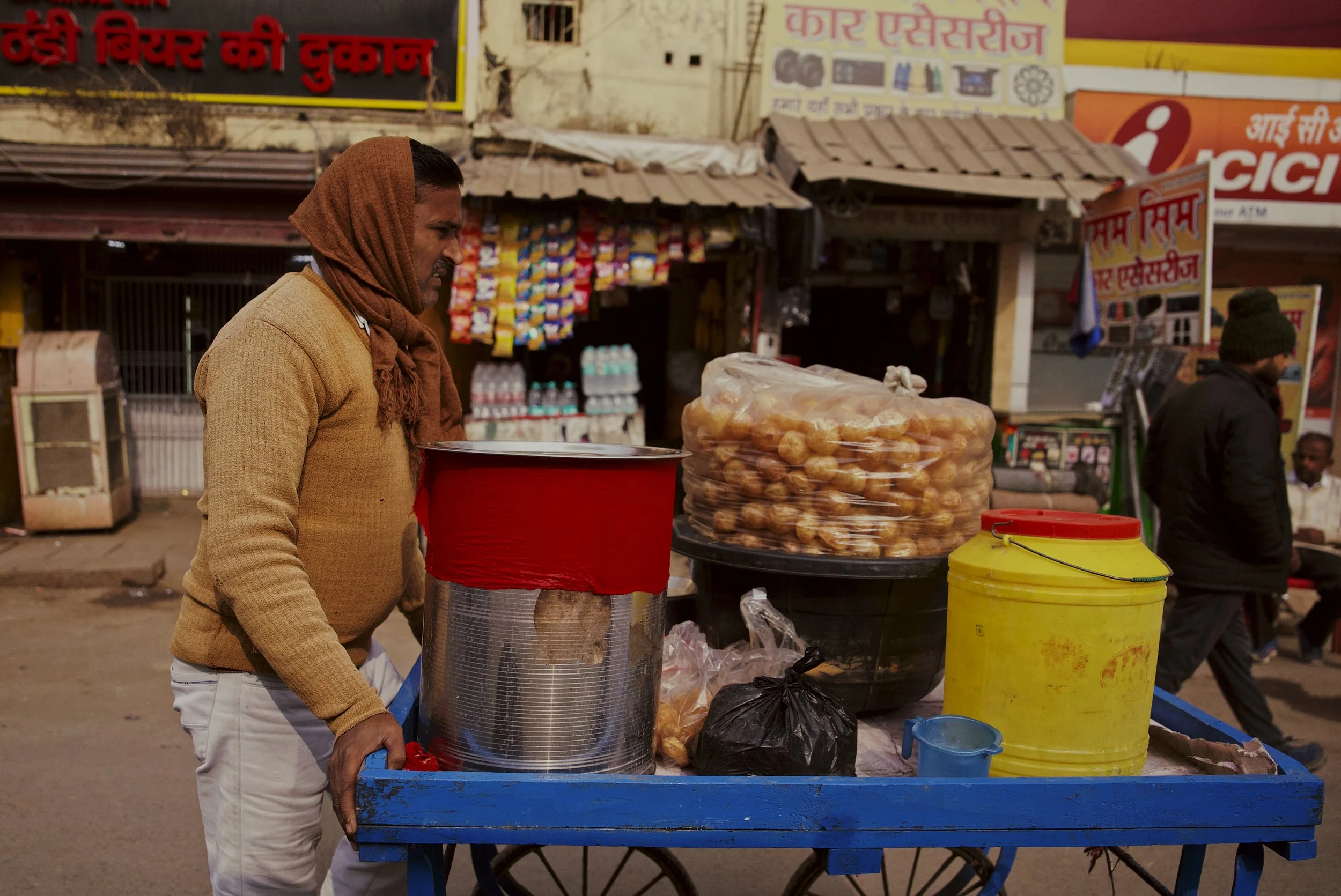 Man sells snacks on the backstreets of Varanasi; December 2025.