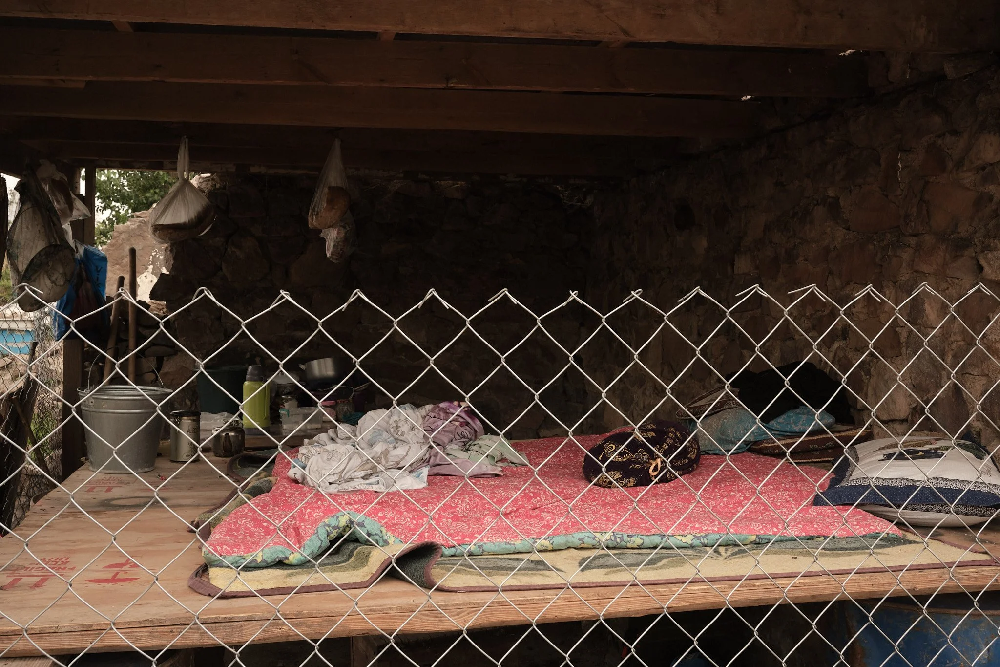 The sleeping arrangements within a destroyed house in Nagorno-Karabakh. Raising the platform off the ground is a precaution against venomous snakes. Food is hung in plastic bags to save it from insects; Nagorno-Karabakh, in a village near Fuzuli, Jul