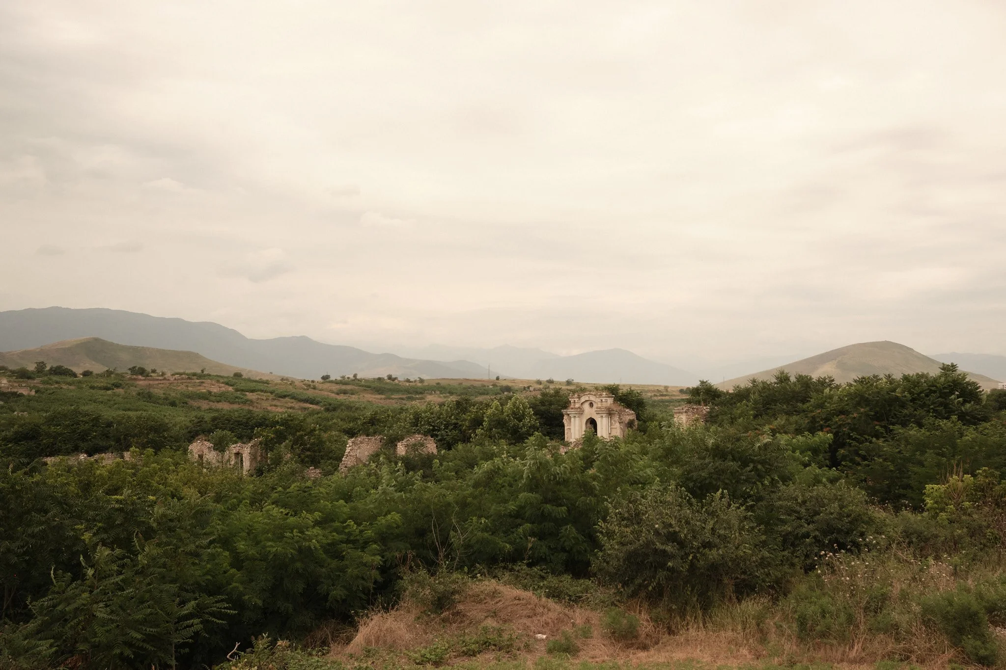 Once-opulent buildings stare back through the undergrowth; Nagorno-Karabakh, July 2026.