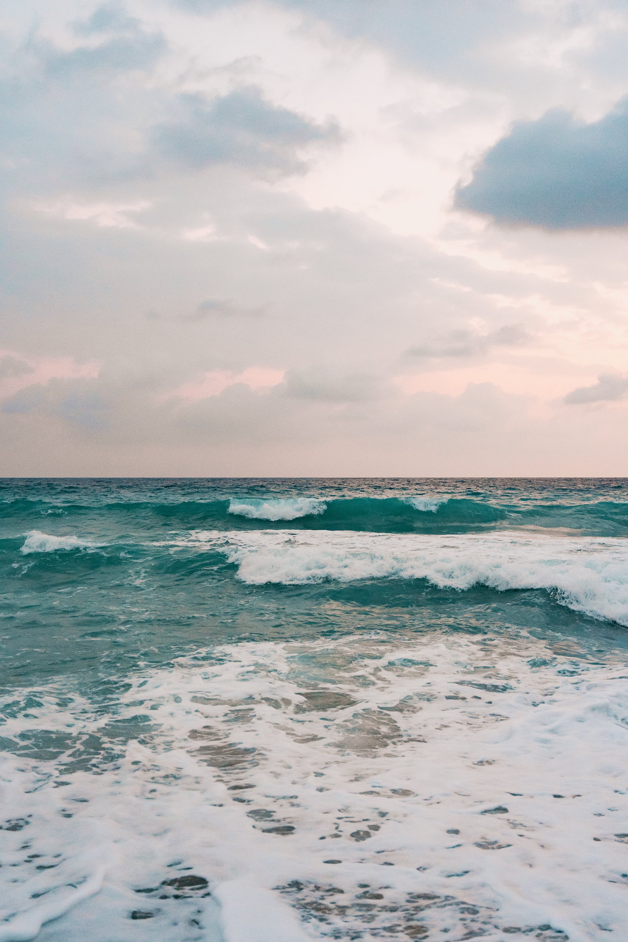 Photo of ocean waves with clouds in the sky during sunset or sunrise.