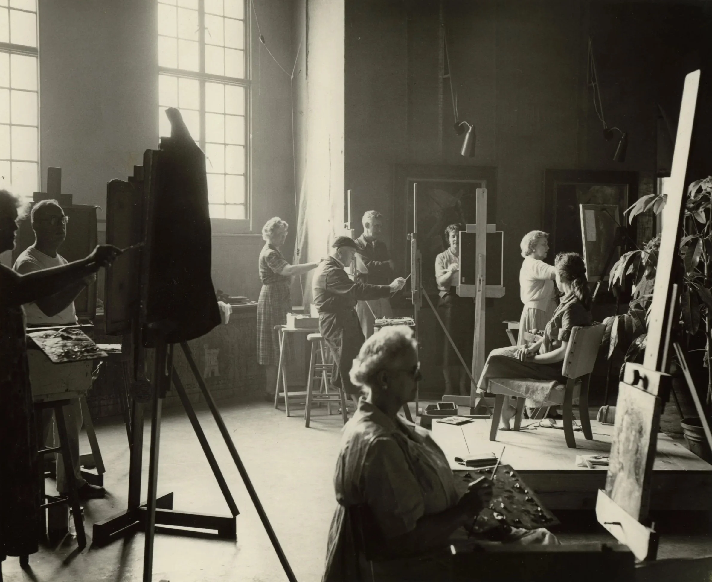 Black and white photo of a life drawing class with models and multiple artists sketching in an art studio.
