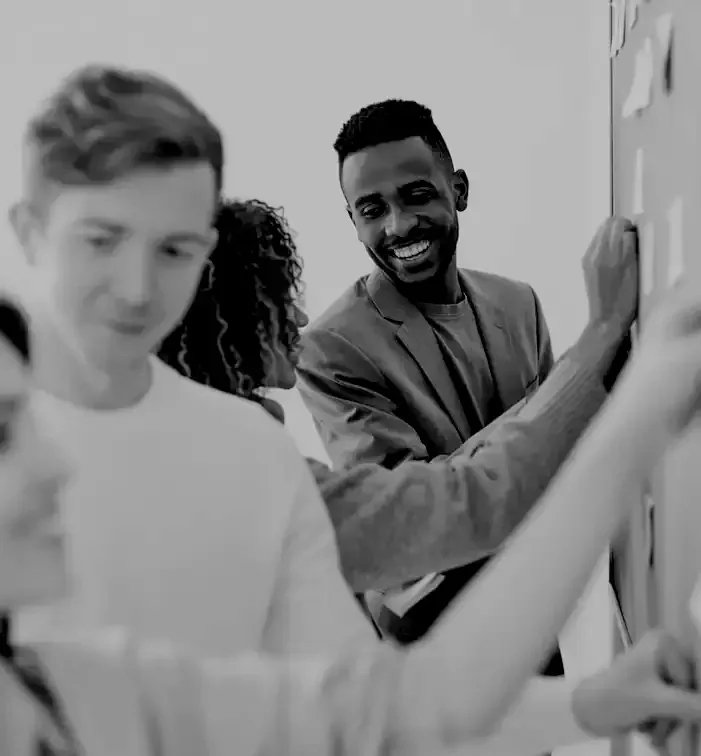 Groupe de trois personnes travaillant ensemble, avec un homme souriant écrivant sur un tableau blanc.