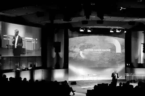 Une conférence avec un homme en costume parlant devant un micro dans une salle sombre.